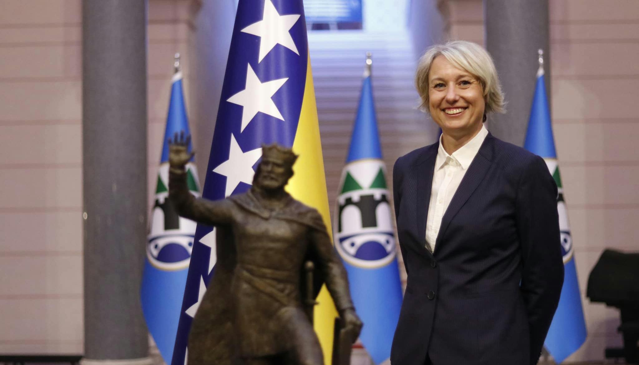 In primo piano sulla sinistra, Anja Margetić, vicesindaca di Sarajevo in abiti istituzionali e sullo sfondo le bandiere della città di Sarajevo.