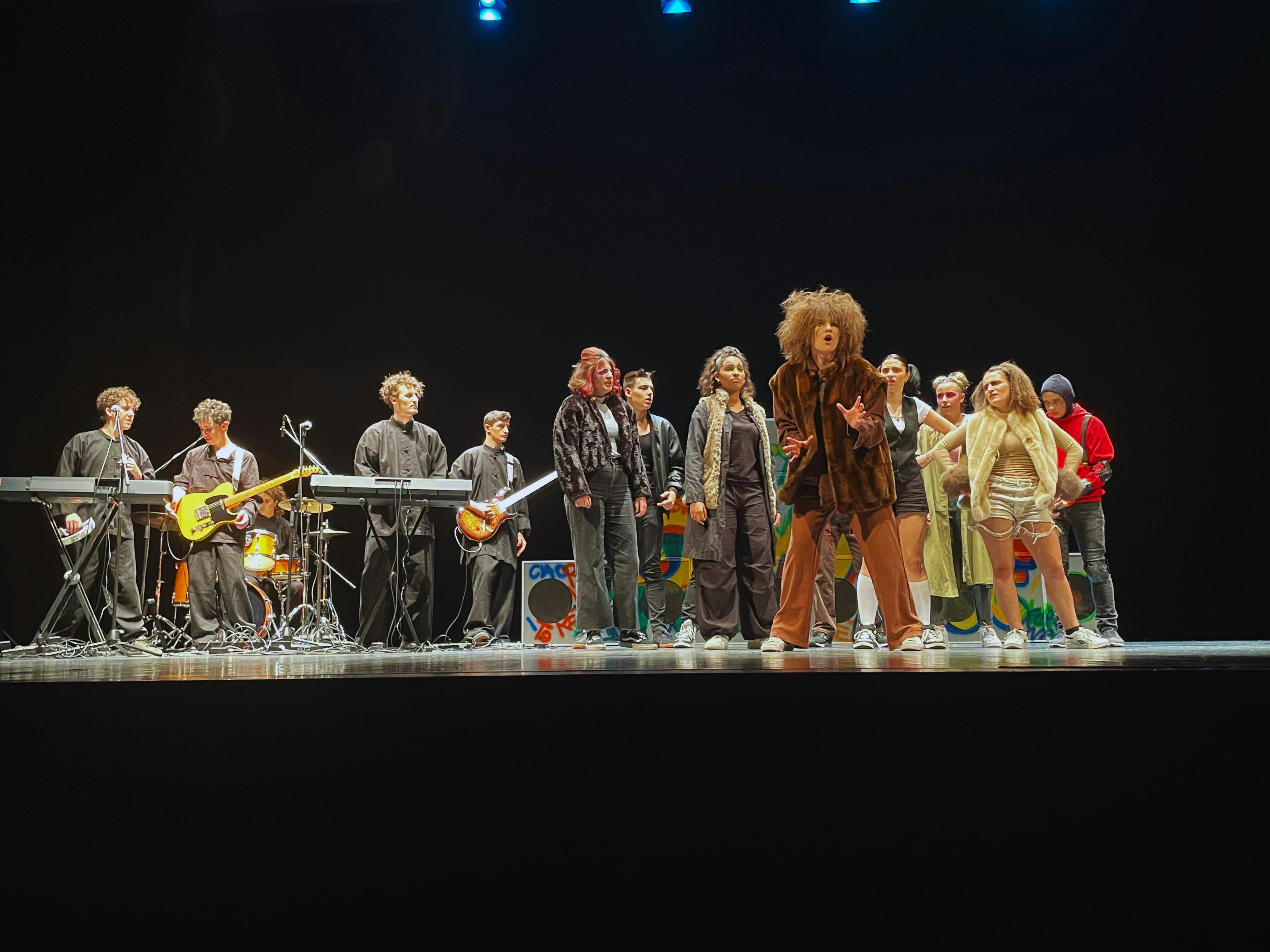 Boys and girls on stage in costumes reminiscent of animals and a band playing