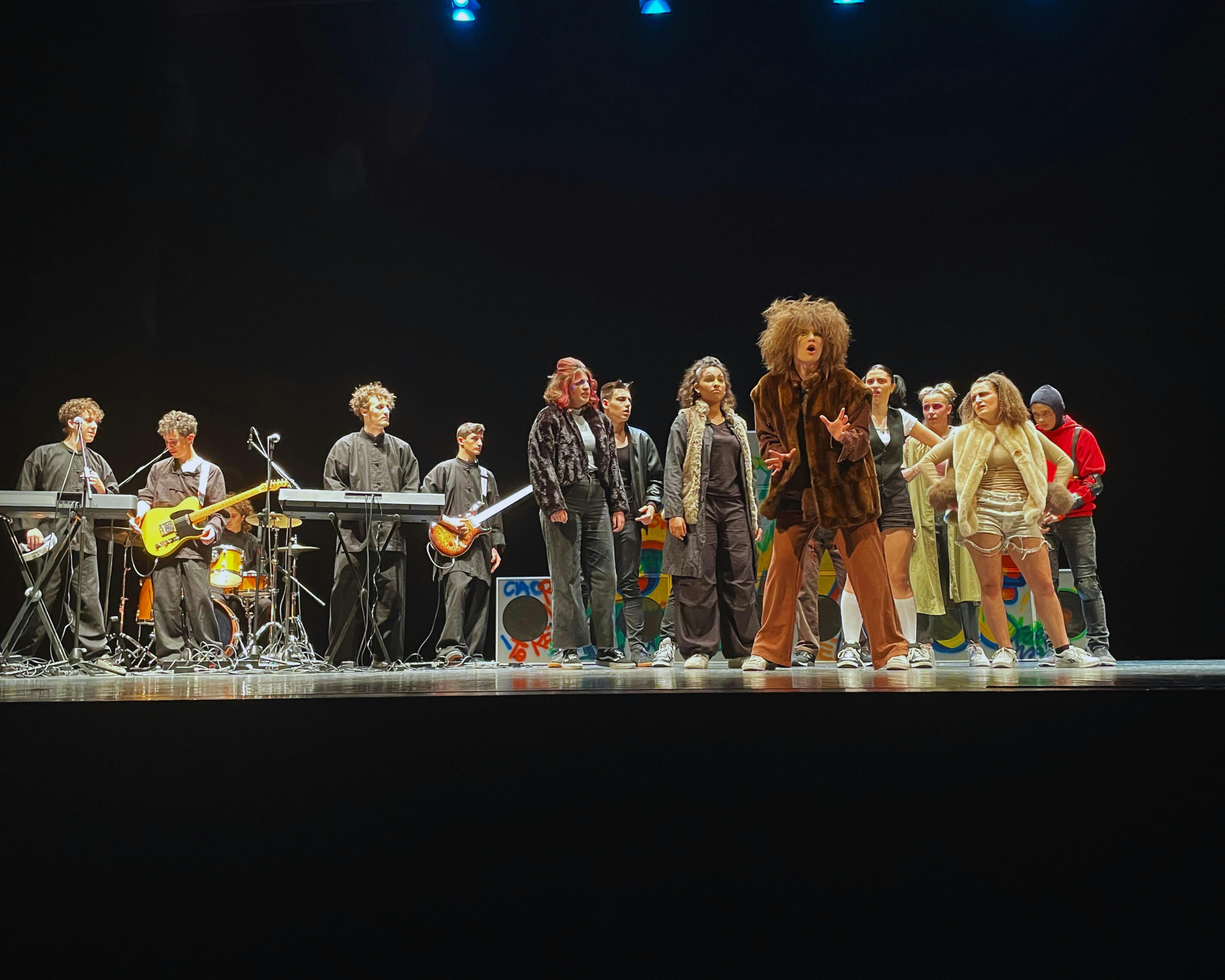 Boys and girls on stage in costumes reminiscent of animals and a band playing