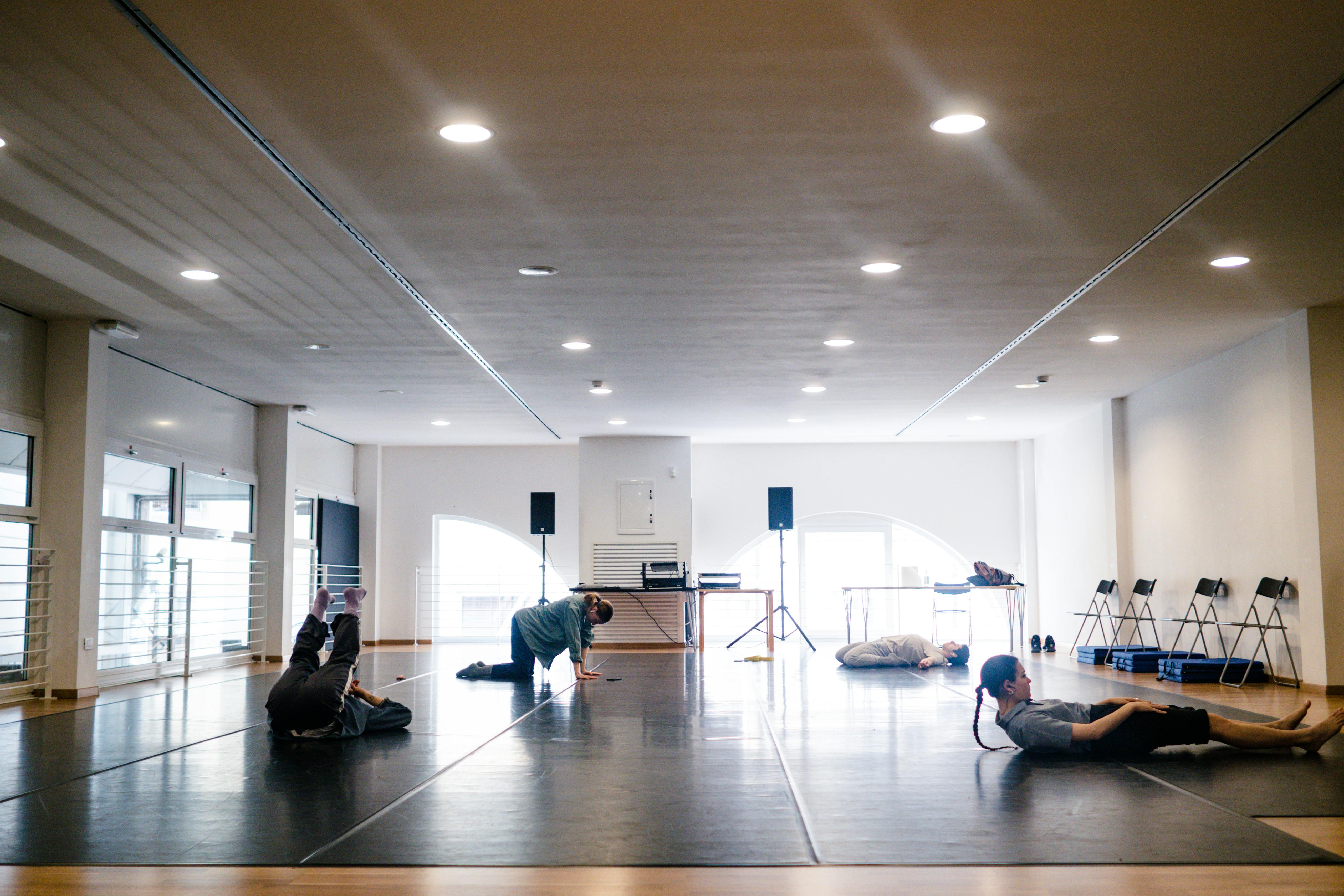 Quattro performer, due ragazze e due ragazzi, in sala, si riscaldano e fanno stretching a contatto con il pavimento