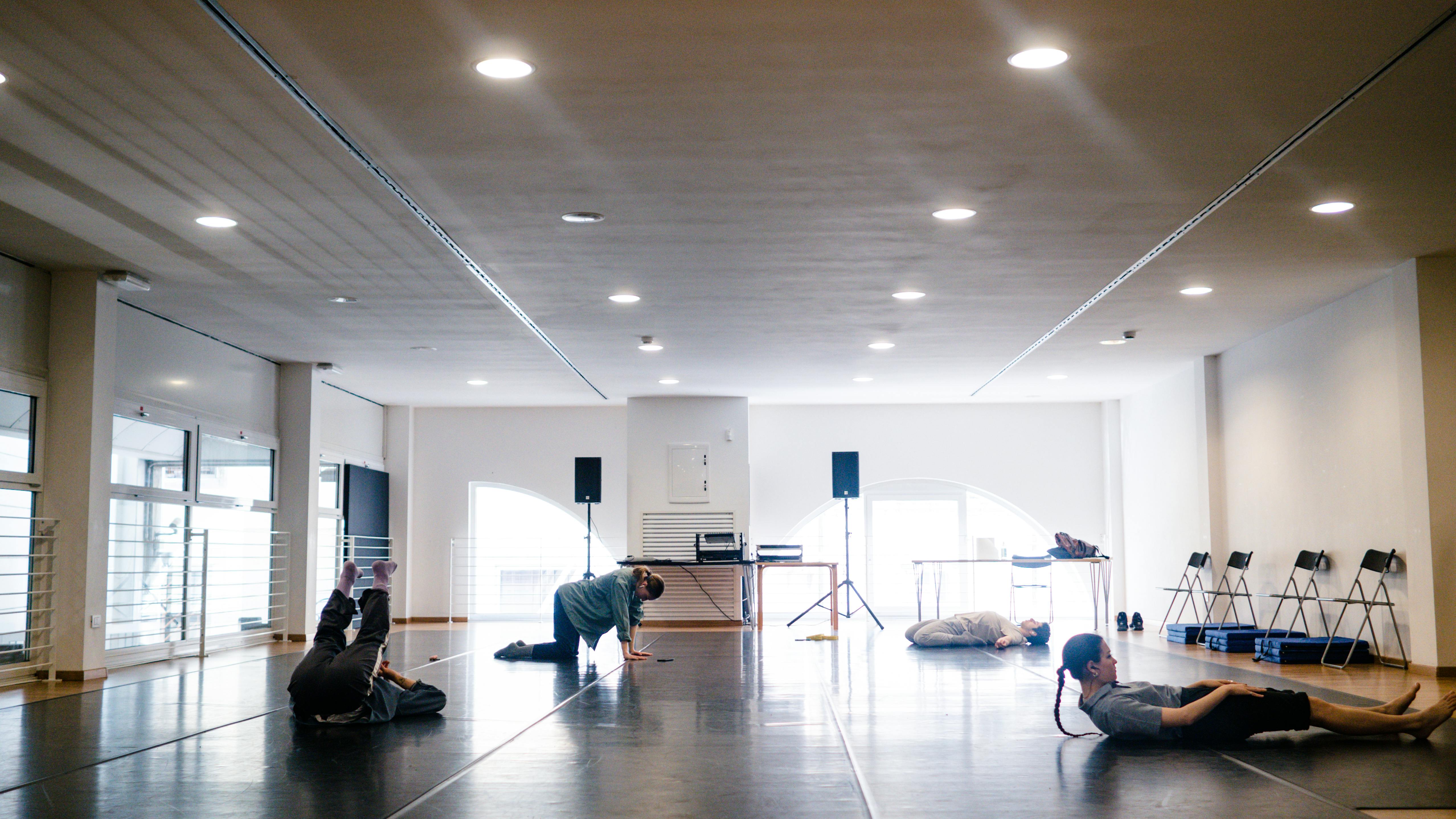Quattro performer, due ragazze e due ragazzi, in sala, si riscaldano e fanno stretching a contatto con il pavimento