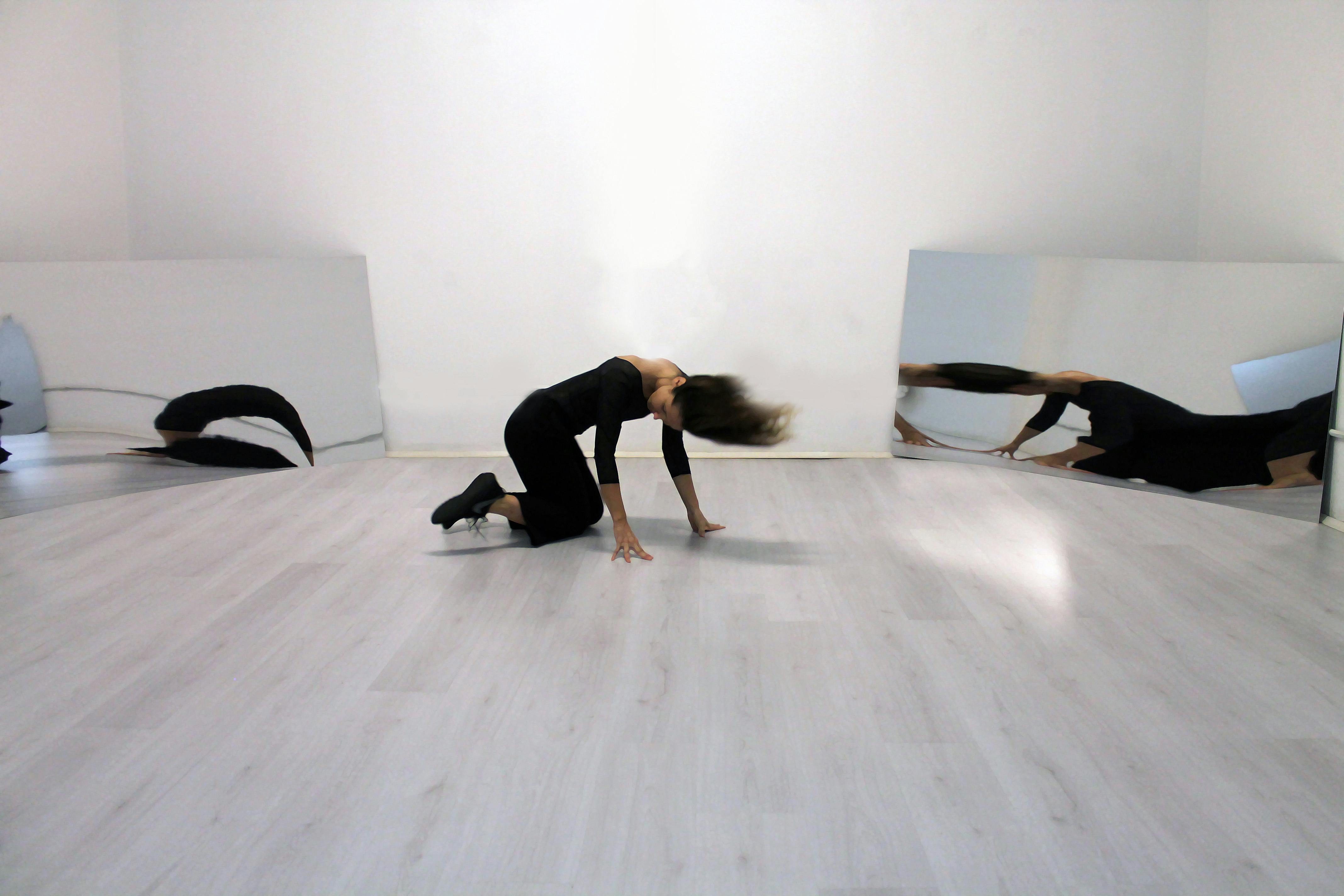 Una danzatrice inginocchiata sembra muovere la testa, due specchi ai suoi lati riflettono l'immagine