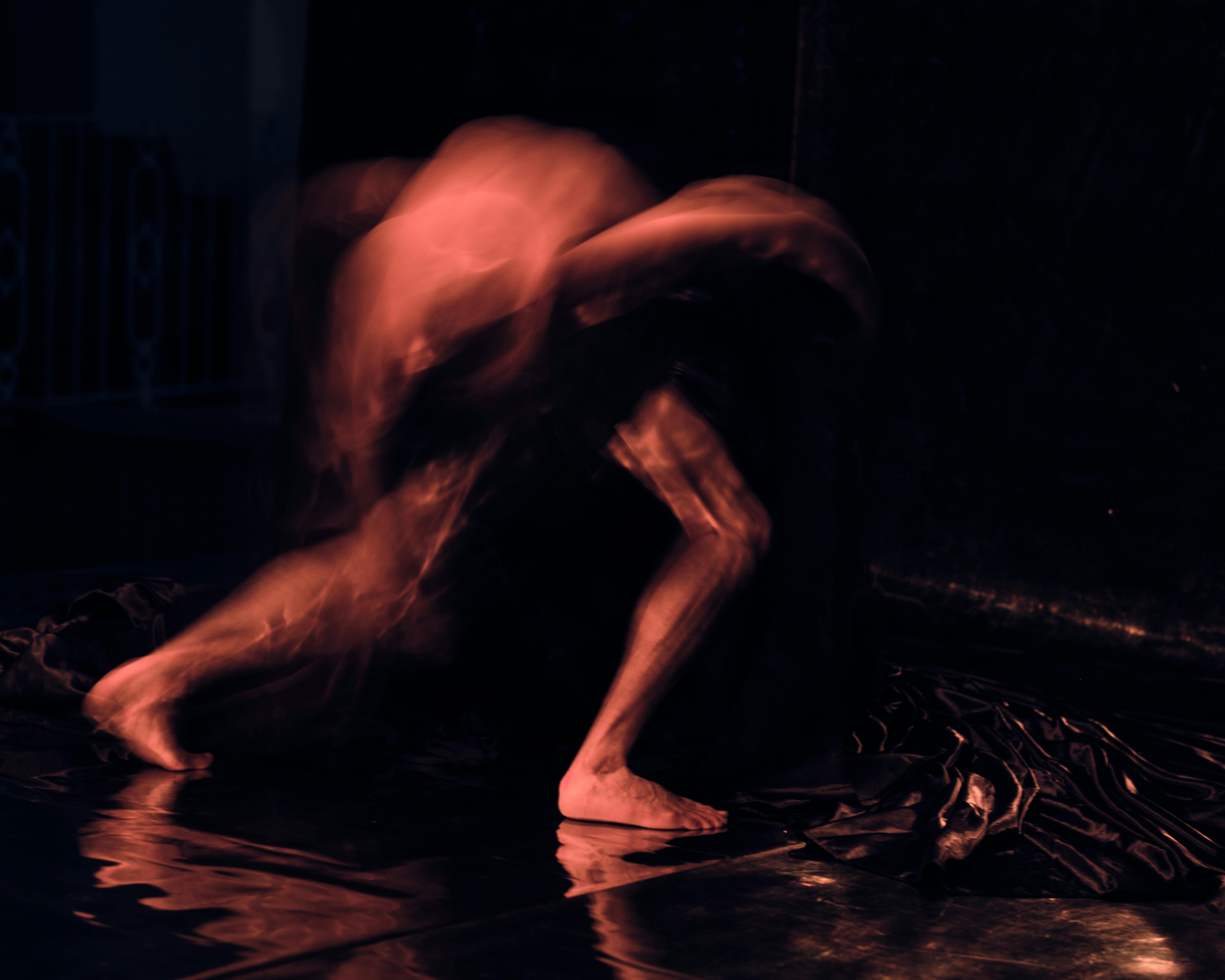 Corpo sfocato in movimento, con il busto rivolto verso il basso su sfondo scuro.