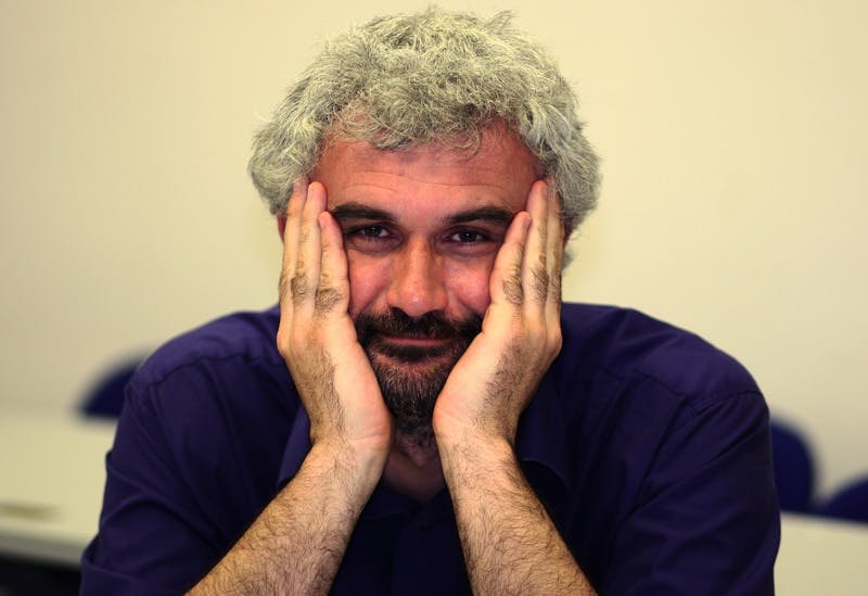 Portrait of Fabio Salomoni. His elbows are resting on the table, with his head in his hands. He has white hair and is wearing a blue polo shirt.