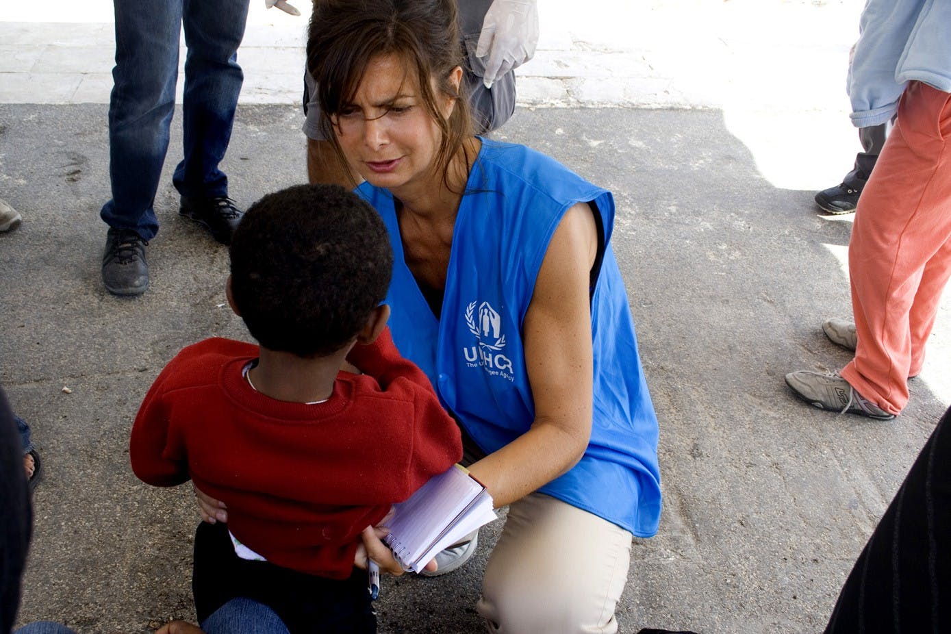 In the photo, Laura Boldrini is kneeling in front of a child and wearing an UNHCR vest.