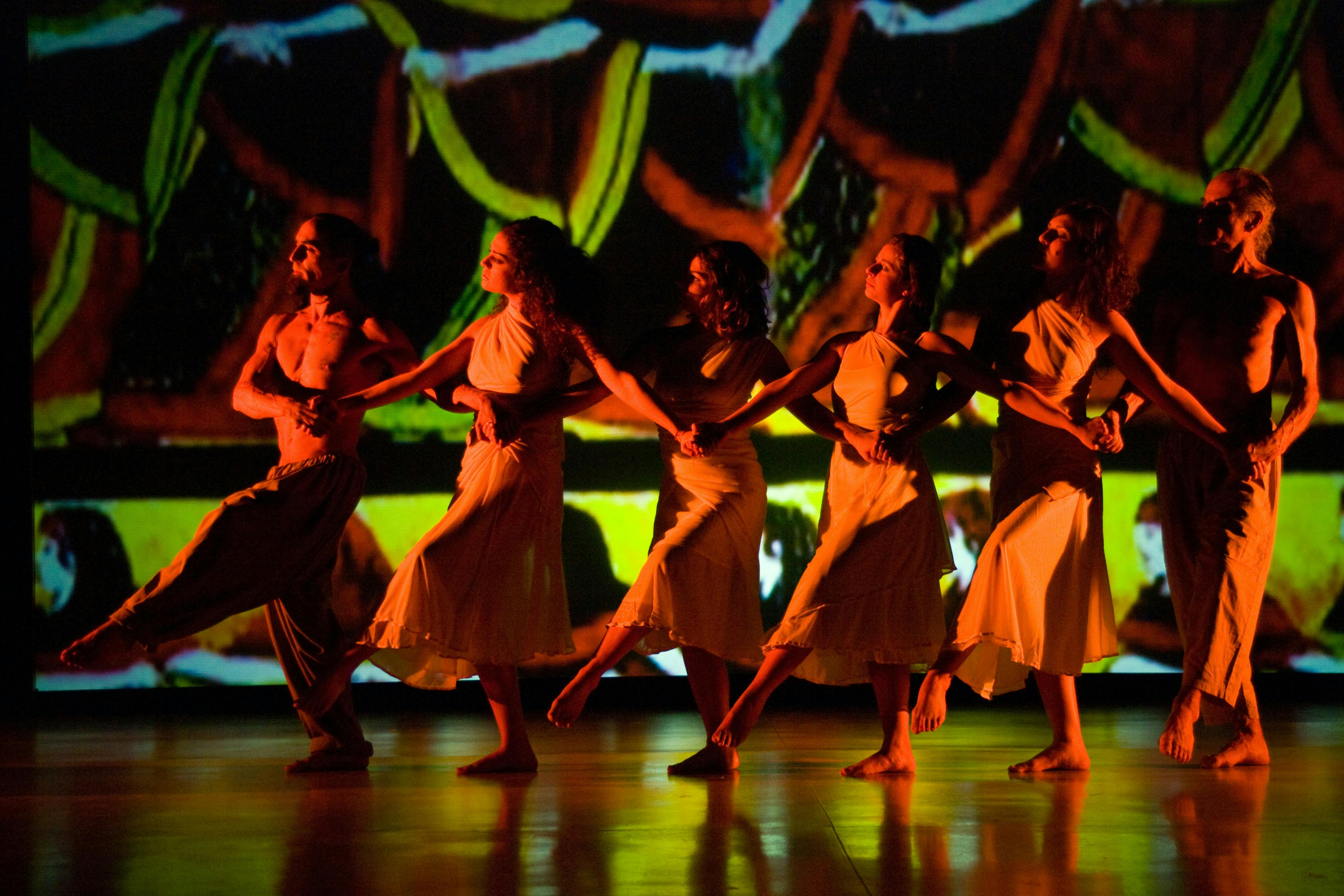 Six dancers, two men and four women. They are standing next to each other, holding hands with their arms crossed.