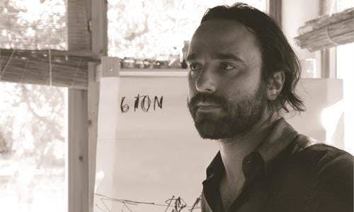 Black and white photo of Thomas Torelli, director and screenwriter. He is looking to his left and has a beard and relatively long hair.