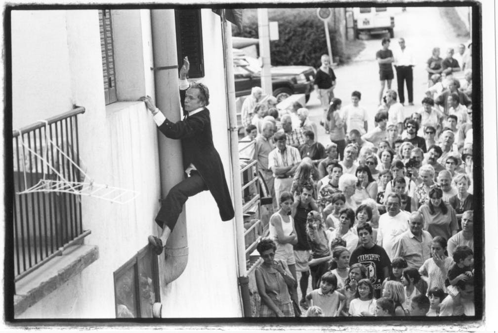 An artist climbs a wall of a house wearing evening attire.