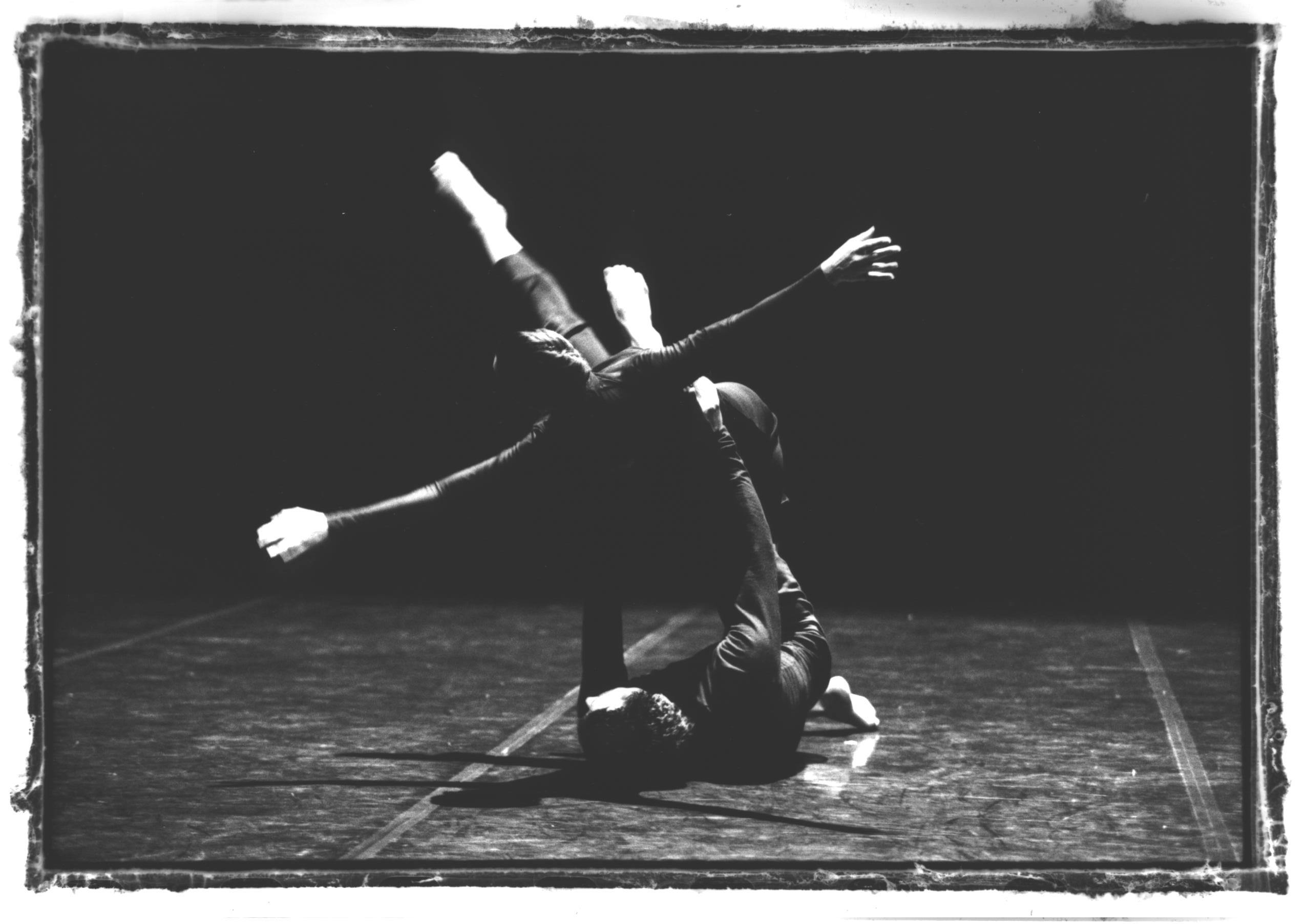 Due artisti in scena, uno sdraiato a terra con le gambe tese in aria. L'altro artista è sollevato e appoggiato alle gambe del primo artista.