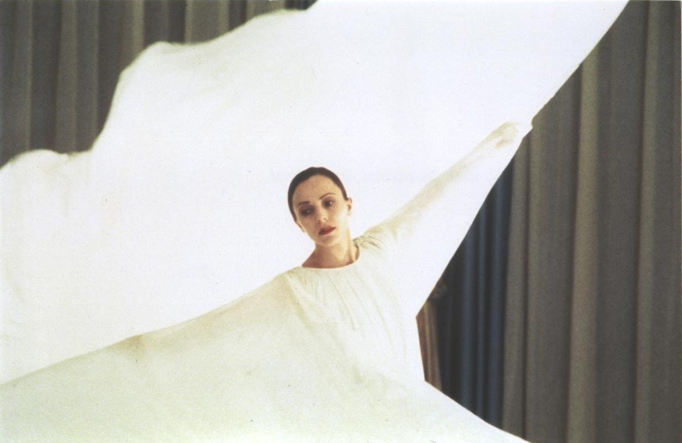 A dancer in a white dress spreads her arms so that the dress expands.