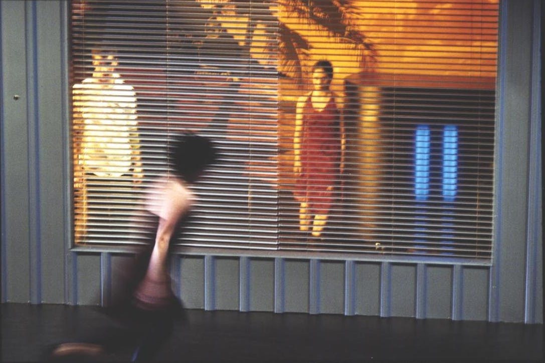 A woman runs blurred. In the background, behind a shutter, two people standing.