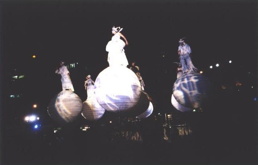 Seven very large spheres suspended in the air. Above each sphere, an artist.