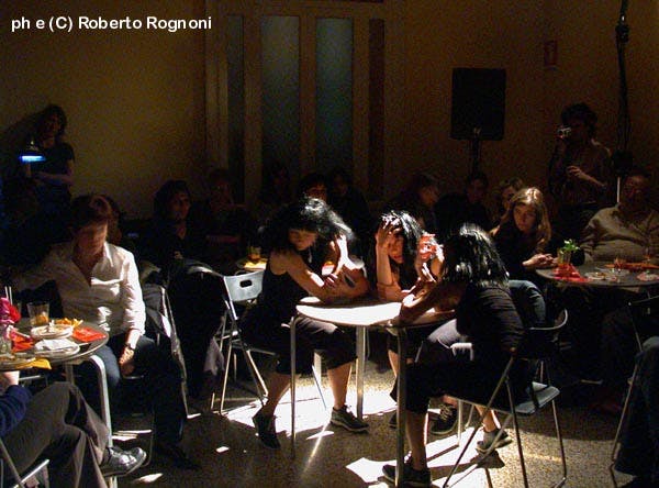 Inside a crowded bar. In the middle of the photograph, a table with three artists dressed in black.