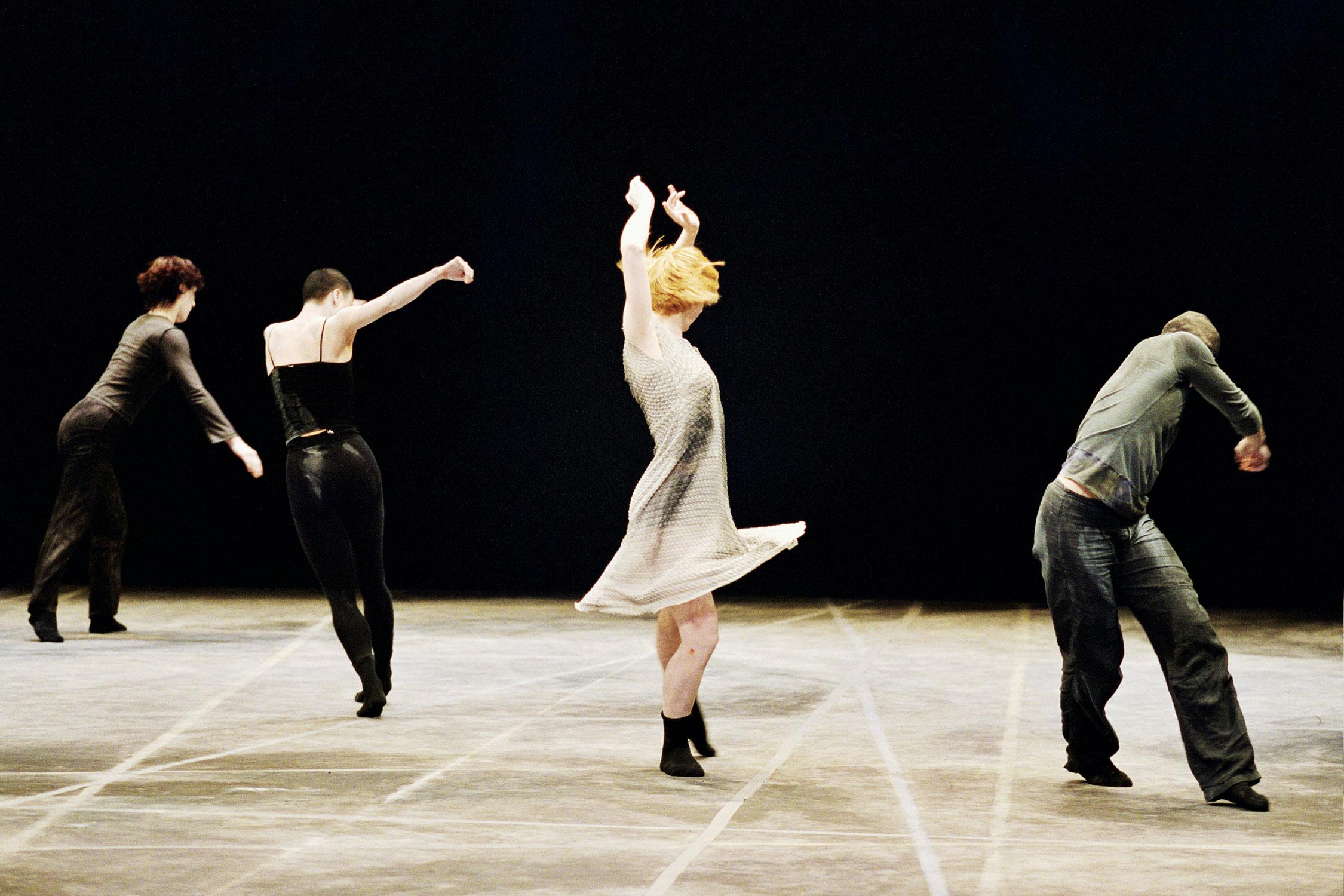 Three artists on stage: one in the center performing a pirouette, and the others jumping in the background.