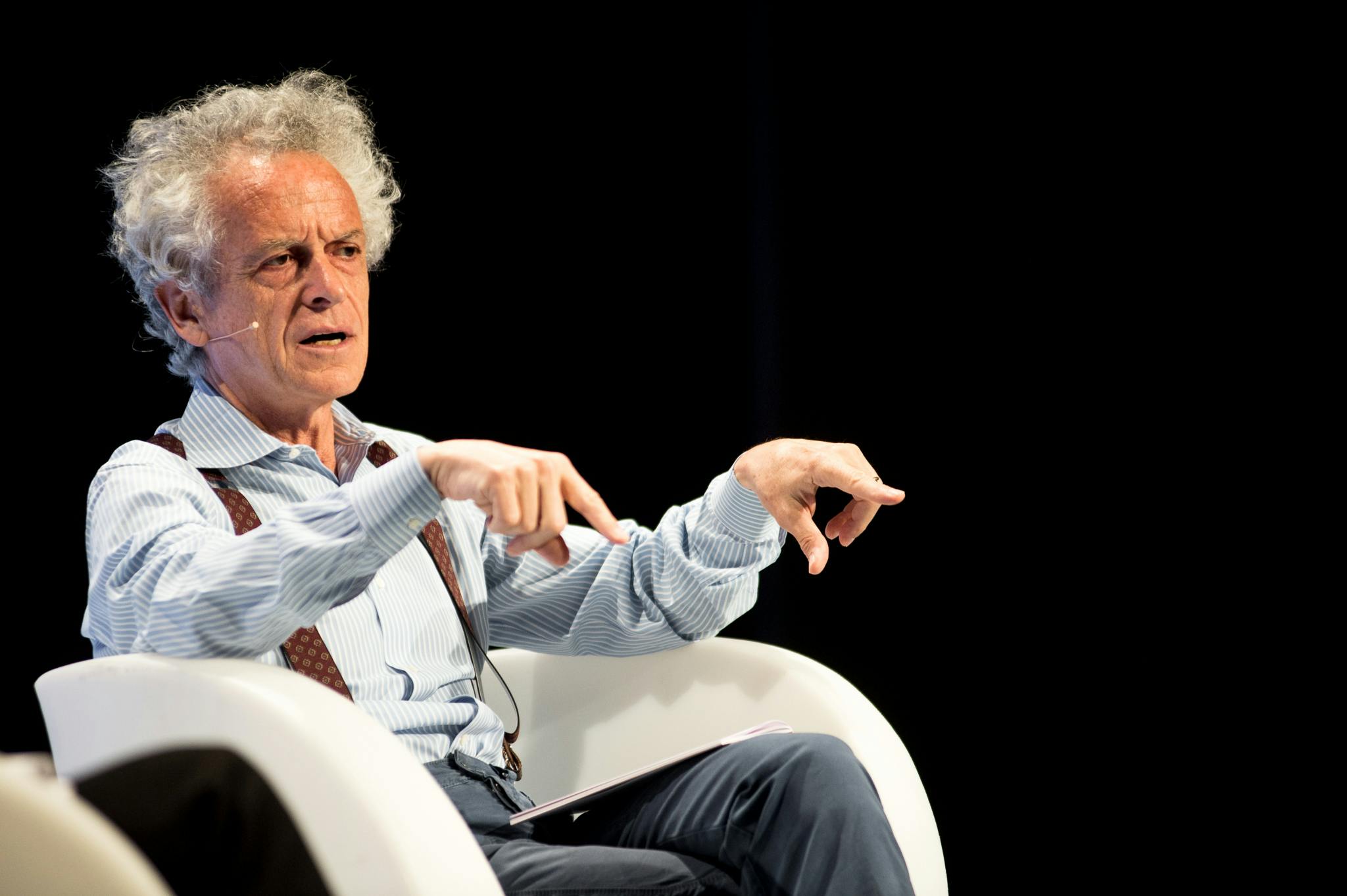 Federico Rampini on stage, seated in an armchair. He is speaking while gesturing with his hands.