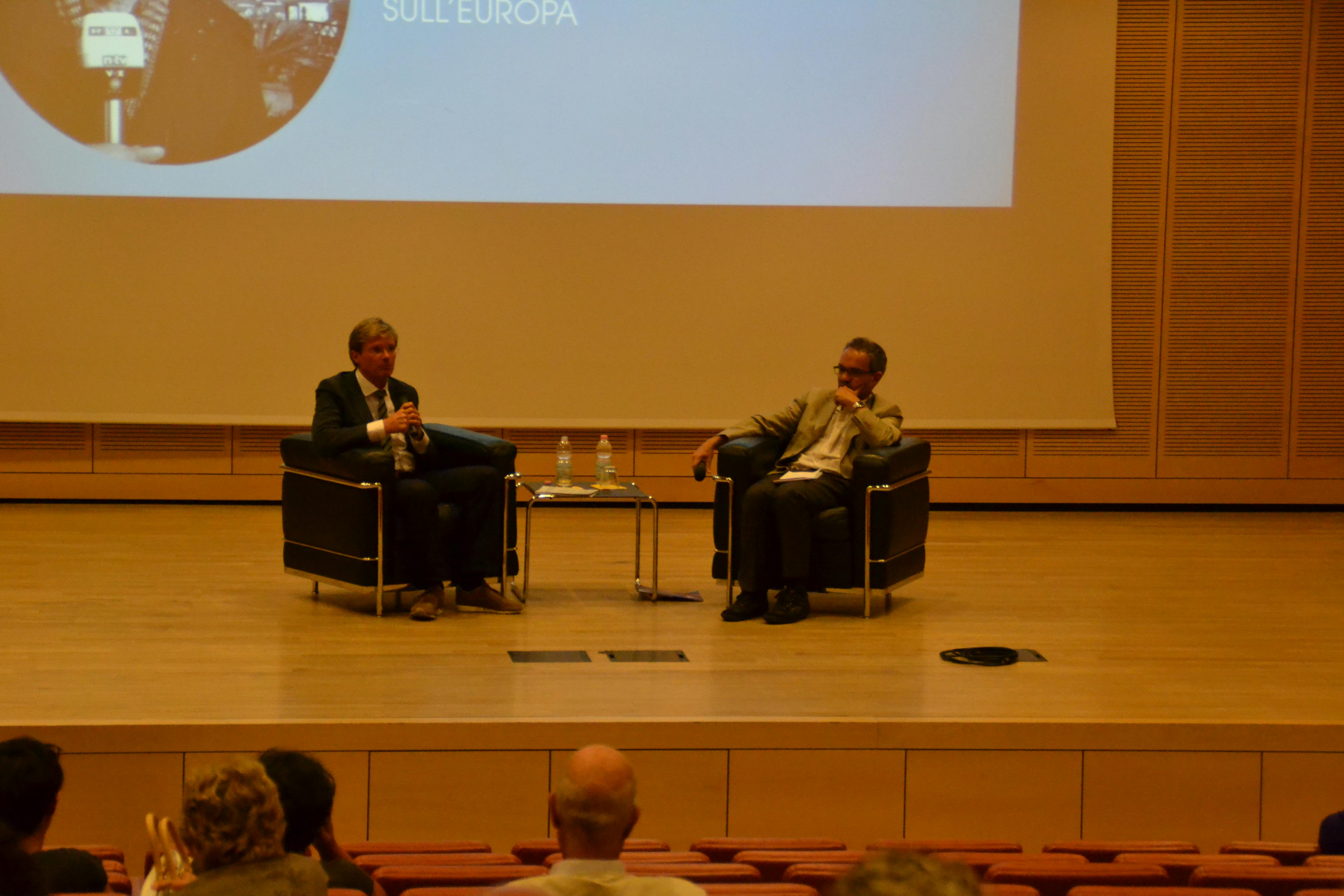Foto di Udo Gümpel, giornalista e scrittore e Giuseppe Ferrandi,  direttore Museo Fondazione museo storico in Trentino mentre parlano seduti su due sedie sul palco.