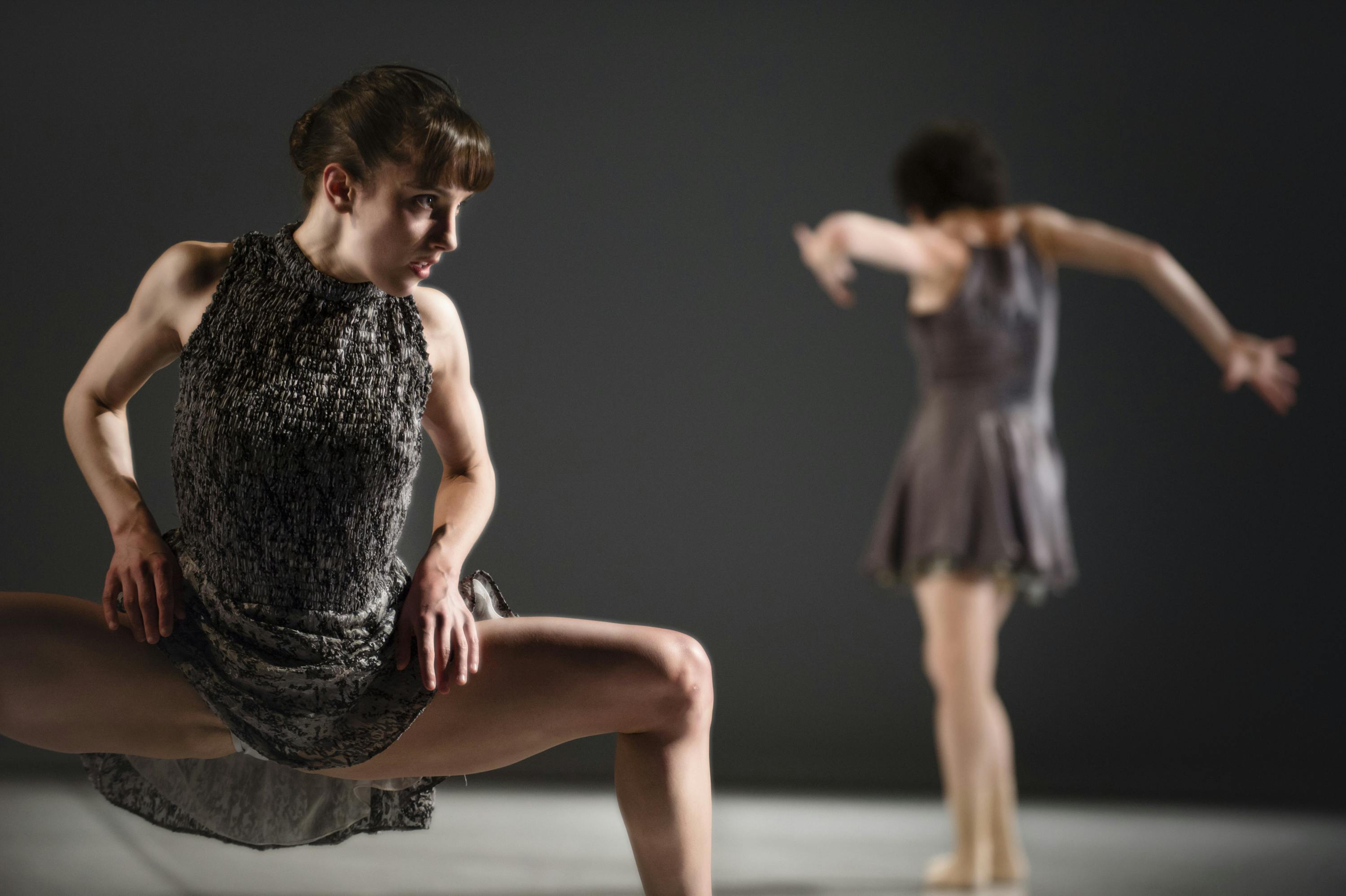 Due ballerine in scena. Una ha le gambe allargate ed è abbassata all'altezza del ginocchio. L'altra è in piedi, di spalle.