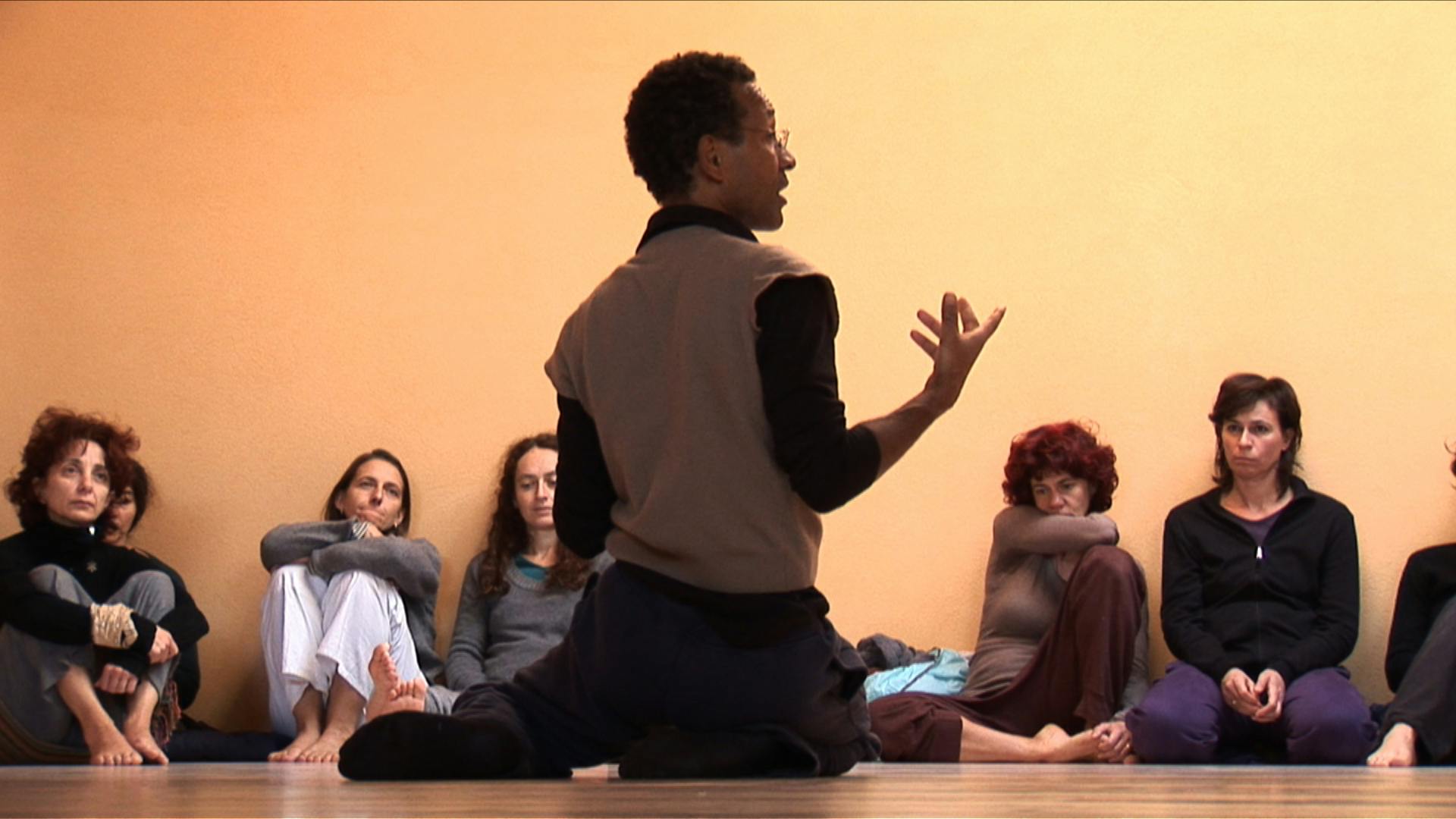 Claude Coldy sitting on the ground with his back to the camera, talking to people