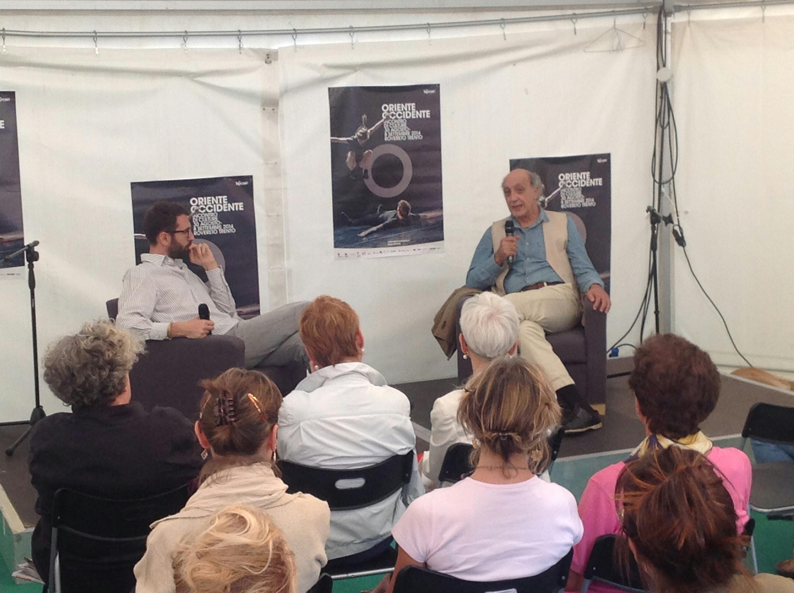 Emanuele Giordana speaking into a microphone while sitting in an armchair in front of an audience