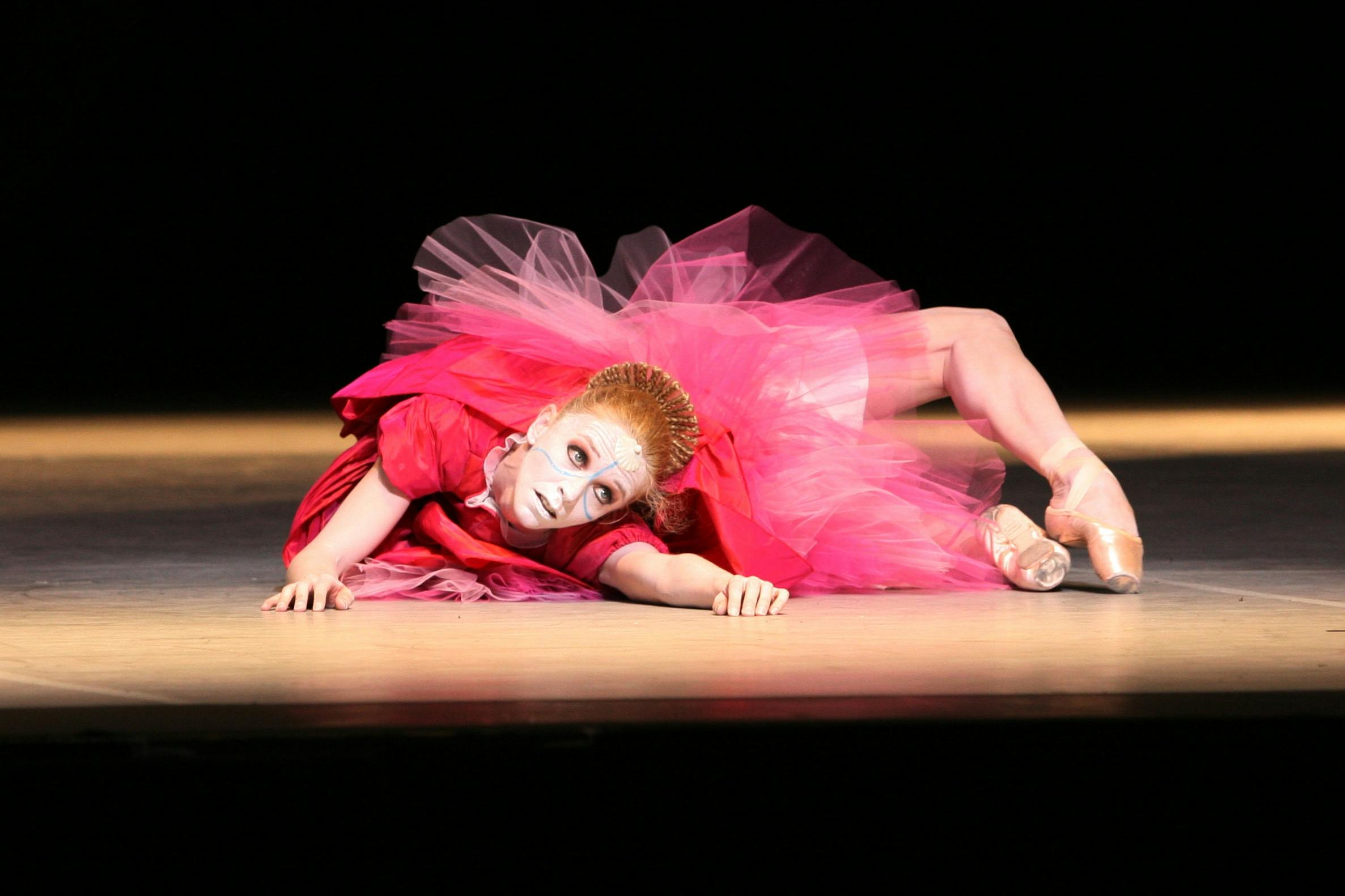 Una ballerina sdraiata a terra. Ha un tutù rosa.