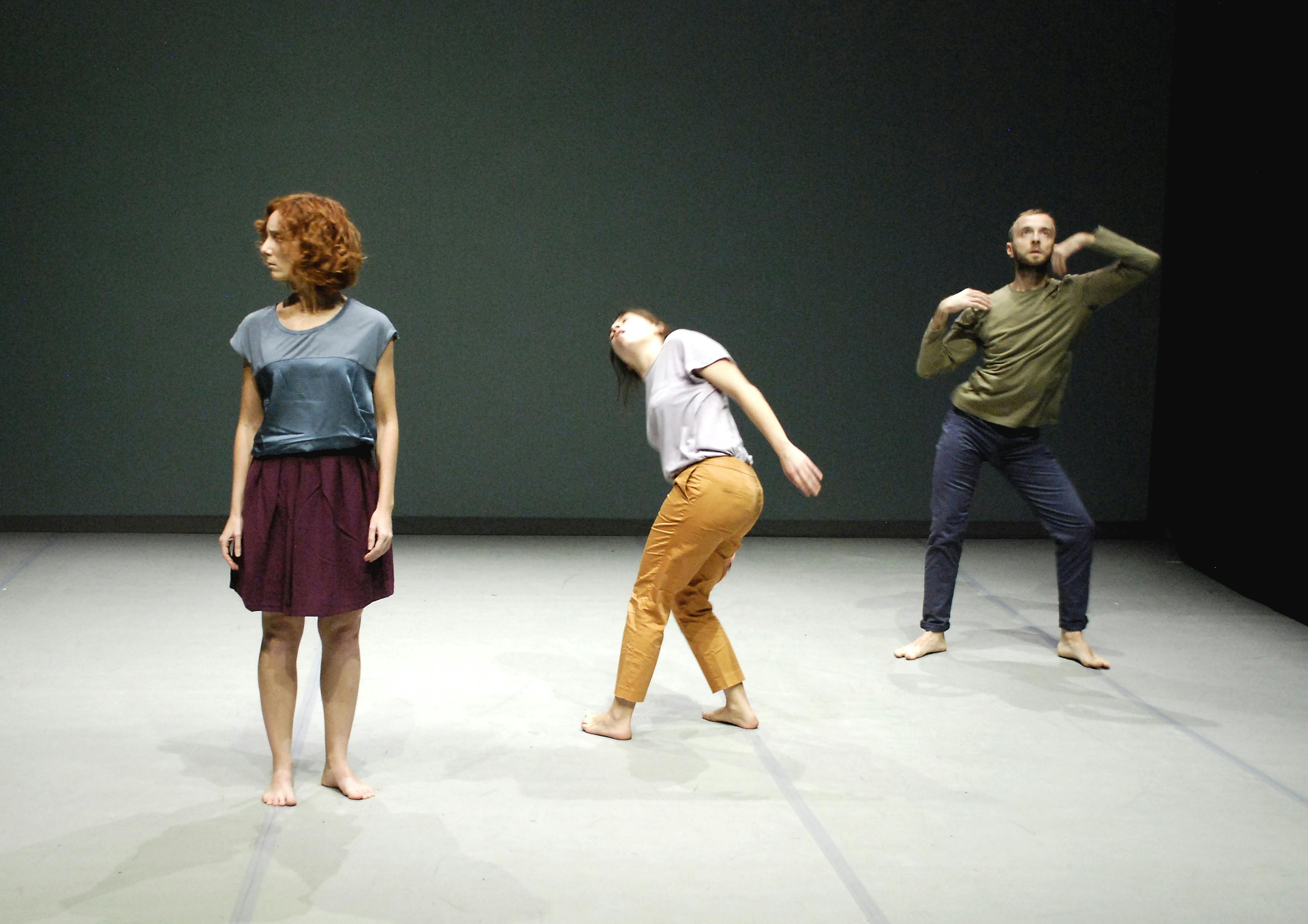 Tre artisti in scena, in pose differenti. A sinistra una è in piedi, guarda alla propria destra; in mezzo un'altra è piegata in avanti e guarda in alto; l'ultimo è in piedi e guarda in alto