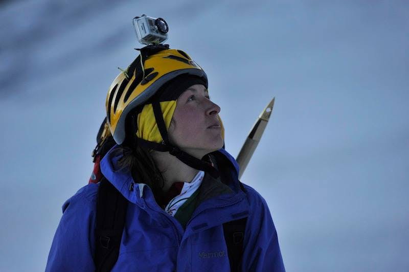 Photo of Eloïse Barbieri. She is in the mountains, wearing a helmet and mountaineering gear, and looking up.