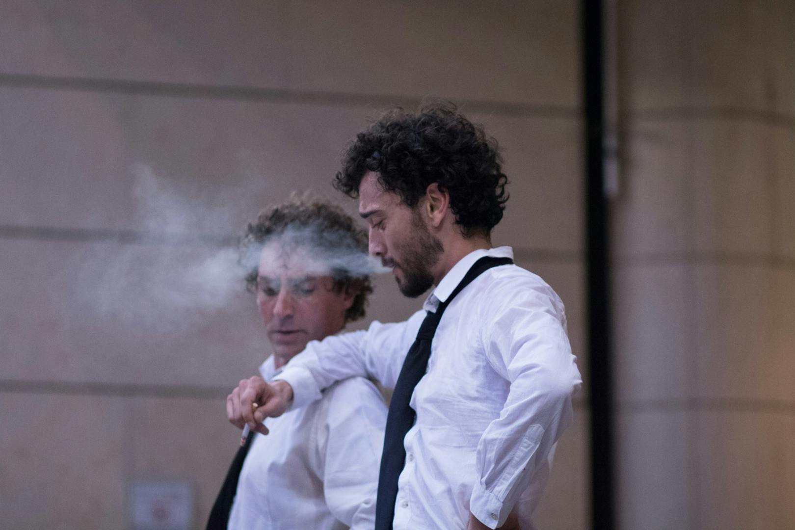 Profile photo of two artists wearing white shirts and black ties. One has his arm resting on the other's shoulder and is smoking a cigarette.