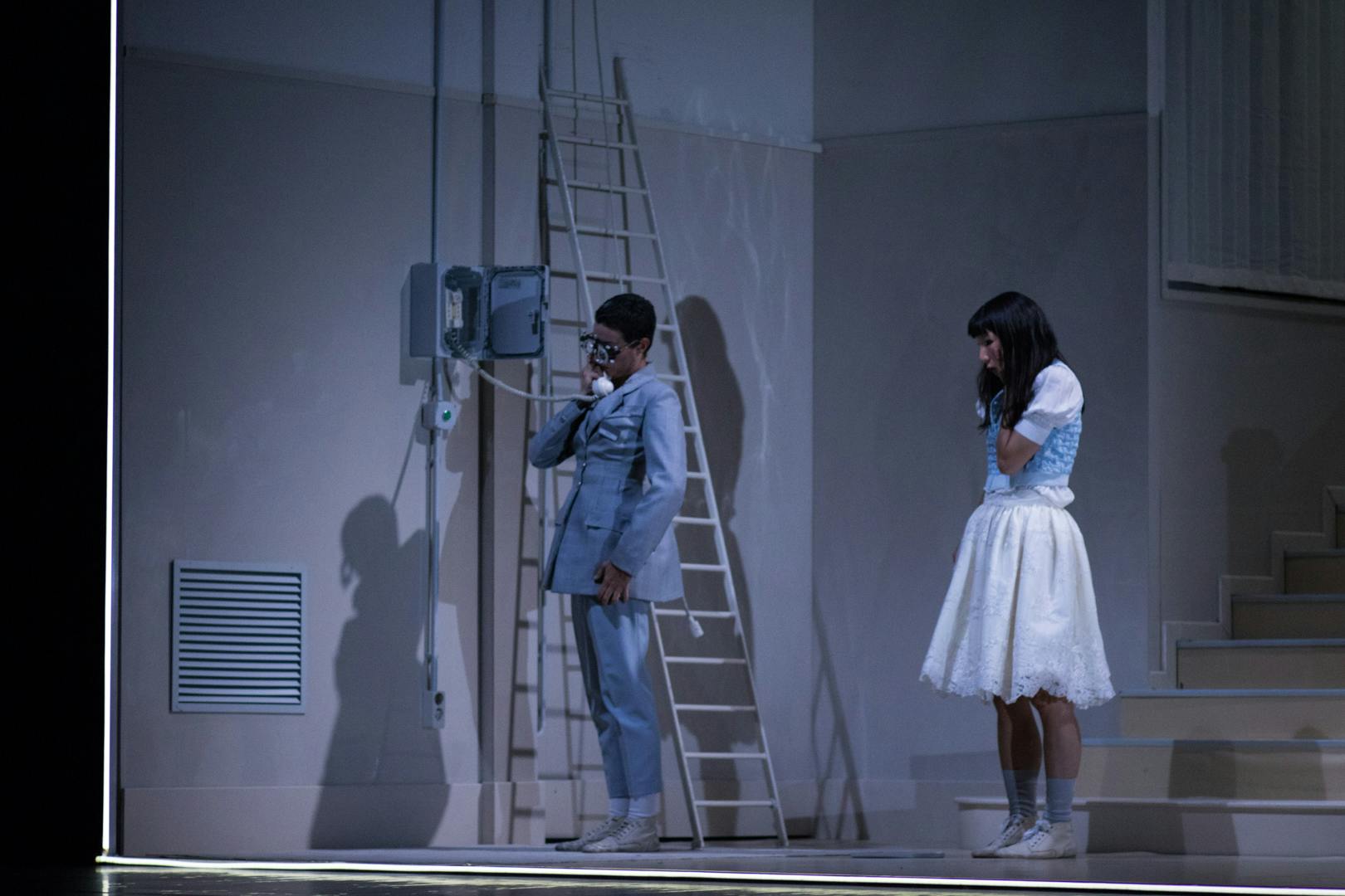 Immagine sui toni dell'azzurro. Due artisti sul palco. Uno è al telefono, l'altra dietro di lui lo guarda.
