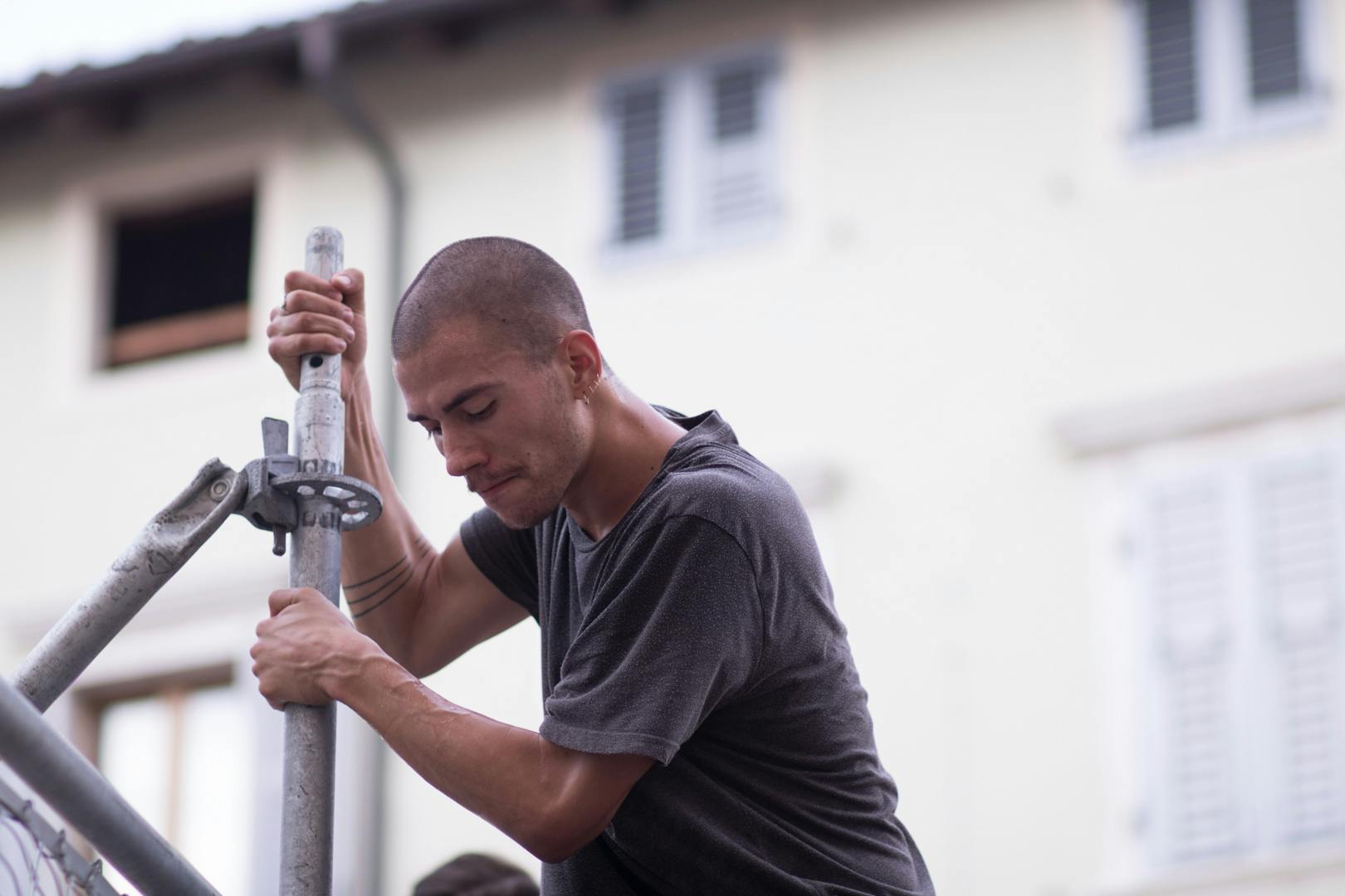 An artist during a performance is attached to a concrete pole. He is wearing a gray t-shirt.