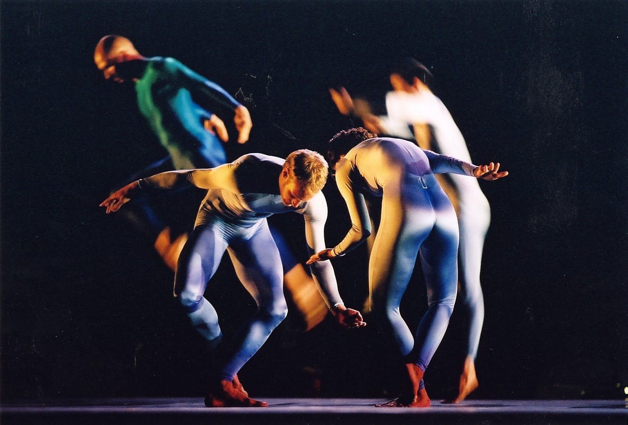 Four dancers wearing colored suits move in space in different directions