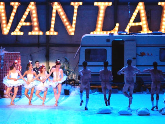 artisti che ballano su un palco, sullo sfondo una scritta led grande e un camper