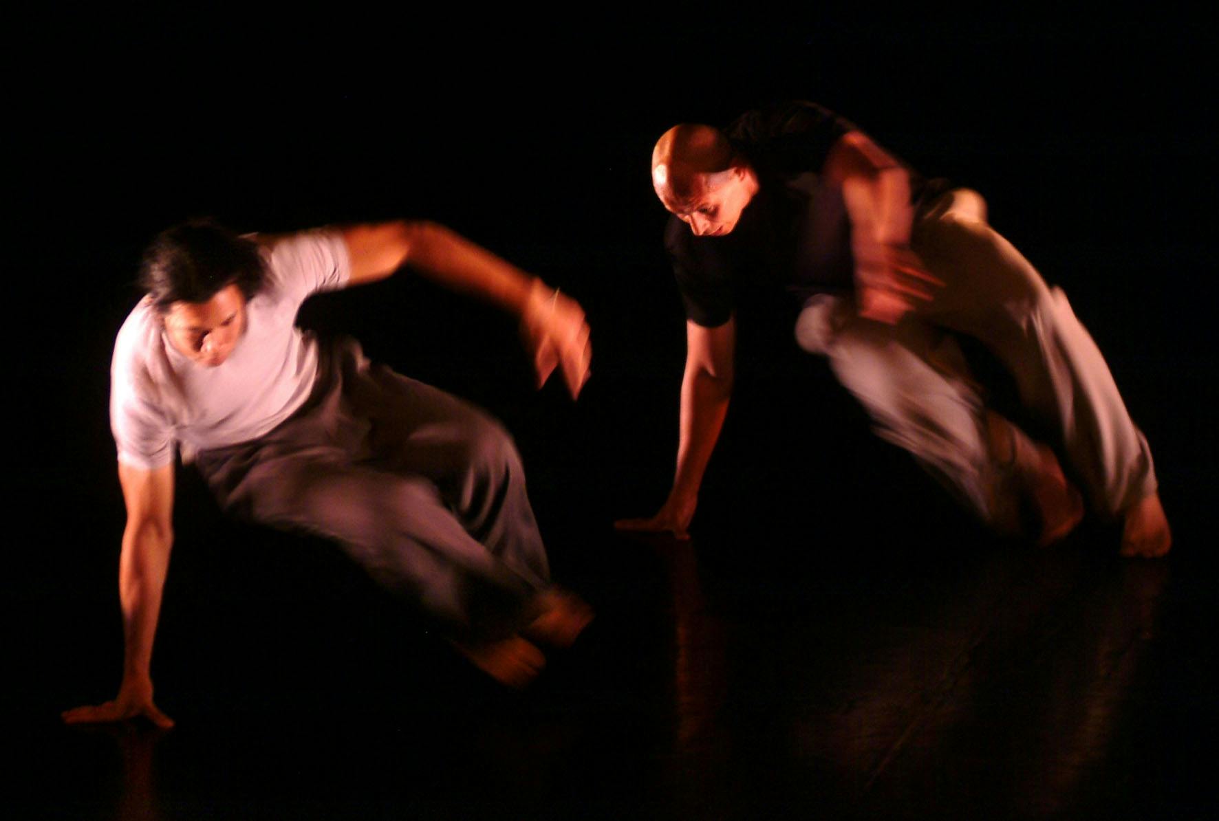 Two dancers, blurred. They support their bodies on their right hand, which is resting on the floor.