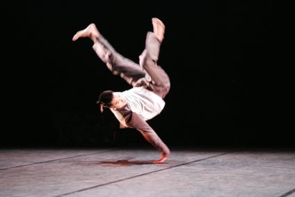 An artist in a hip hop position, upside down leaning on their arm on the ground.