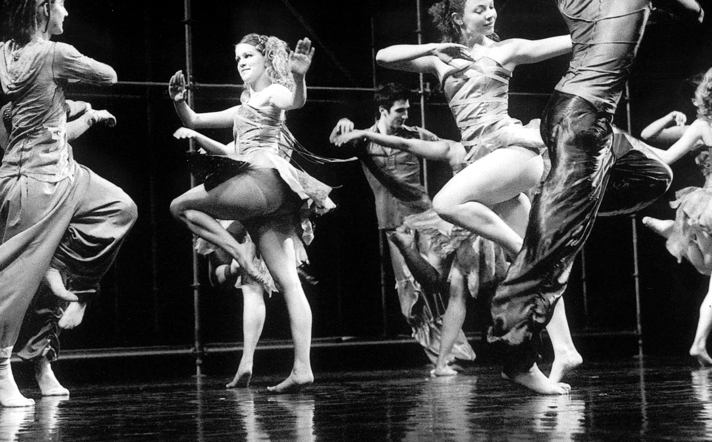 Eight dancers on stage, scattered in random order. They all have the same pose with arms wide open and one leg bent in the air.