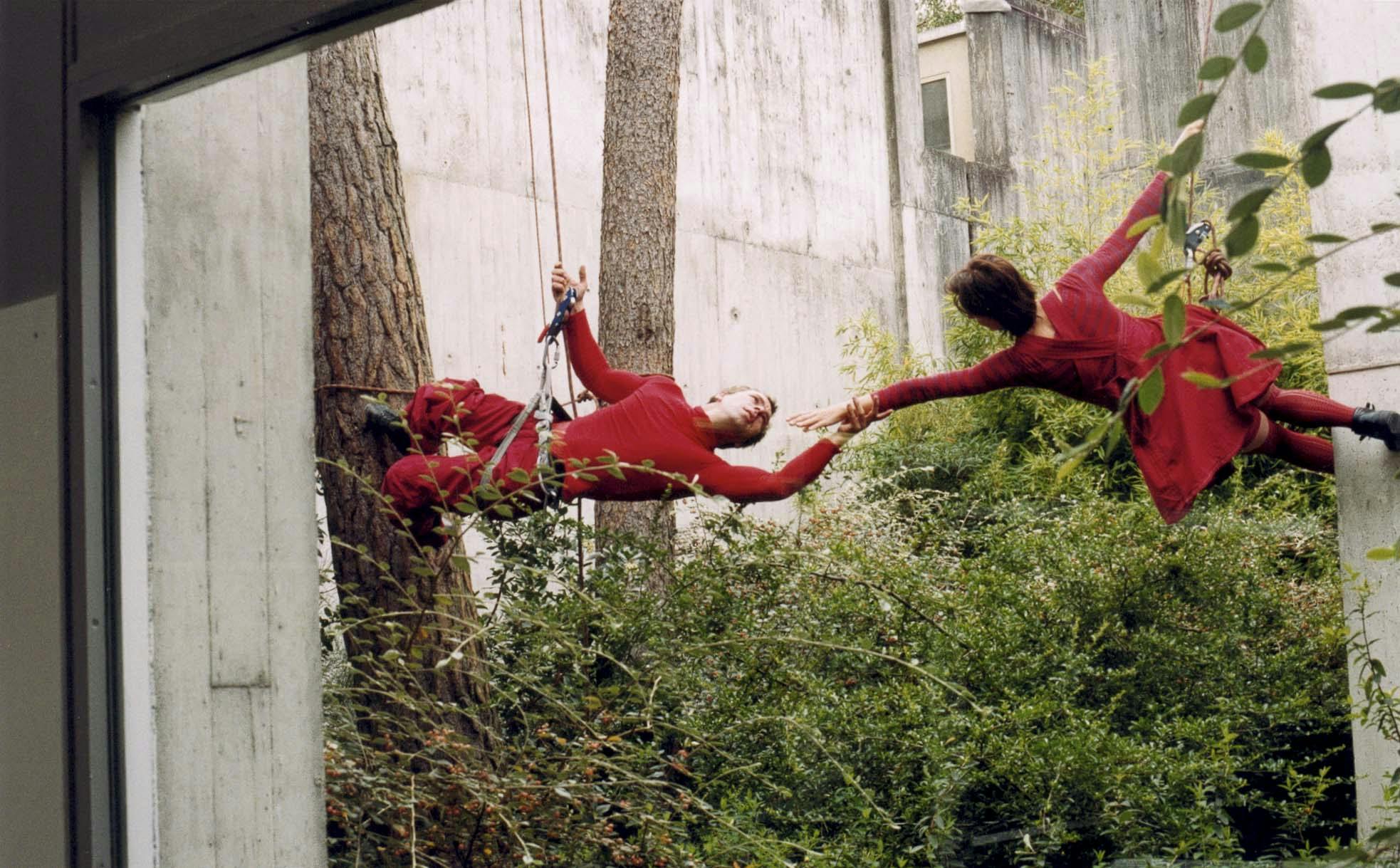 Two artists hanging by a thread from a concrete structure dancing in the air