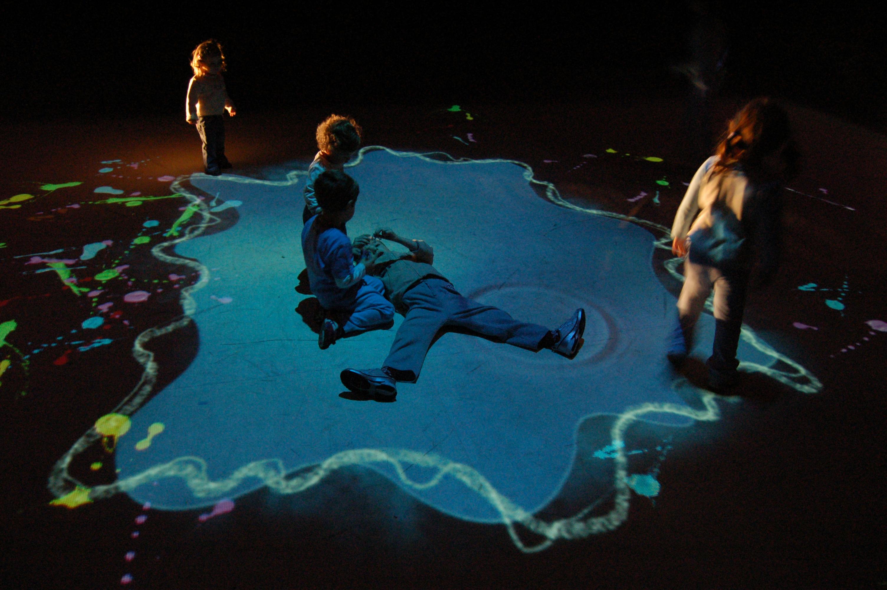 The image portrays people immersed in a colorful installation