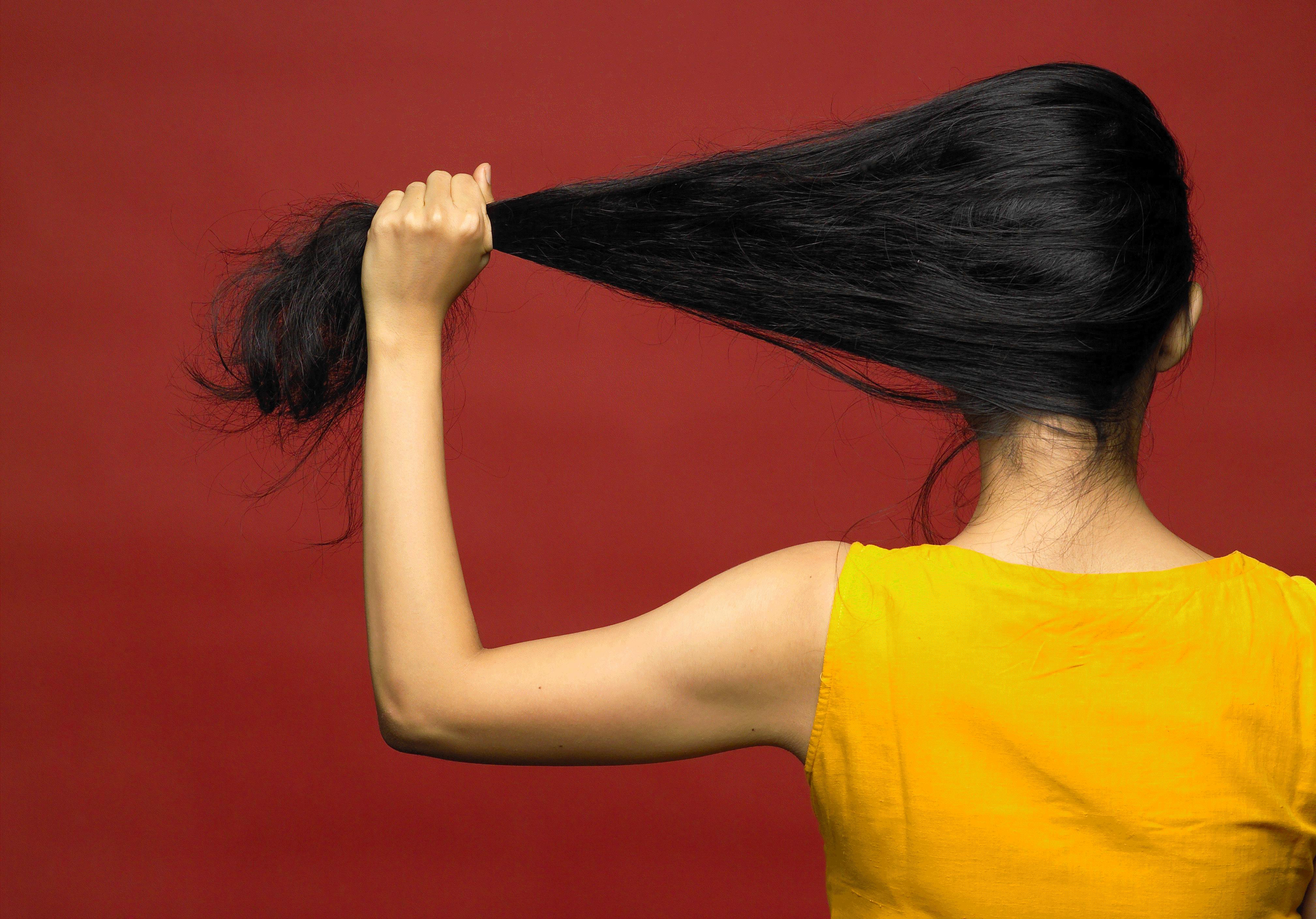 An artist seen from behind is pulling her dark hair to the left, wearing a bright yellow shirt against a vivid red background.