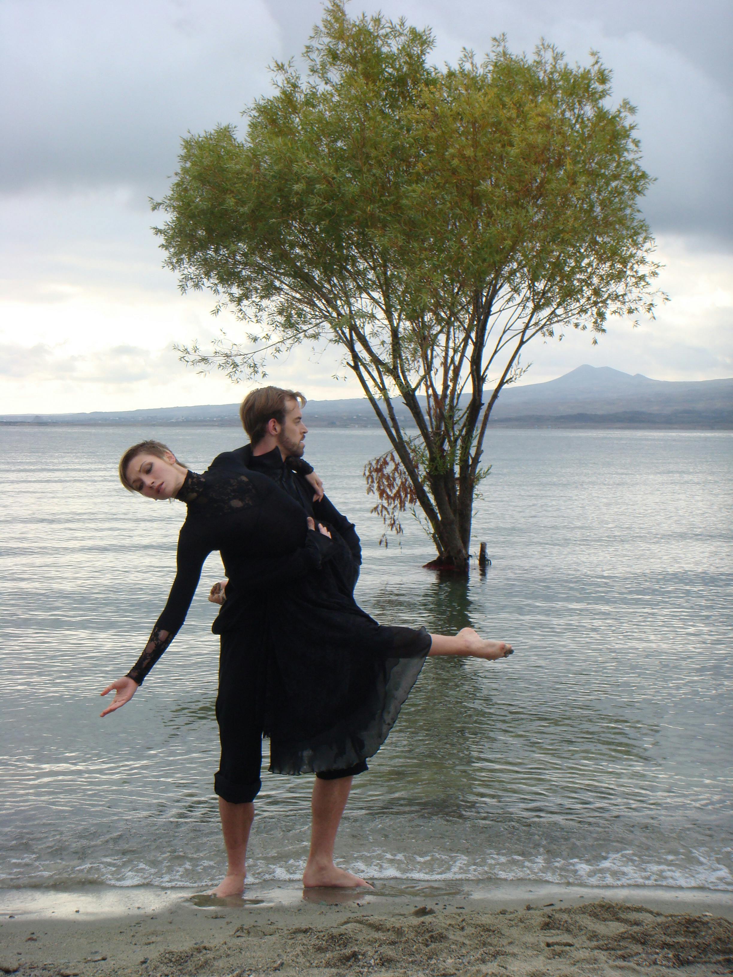 Two artists standing by the shore of a lake dancing in black outfits.