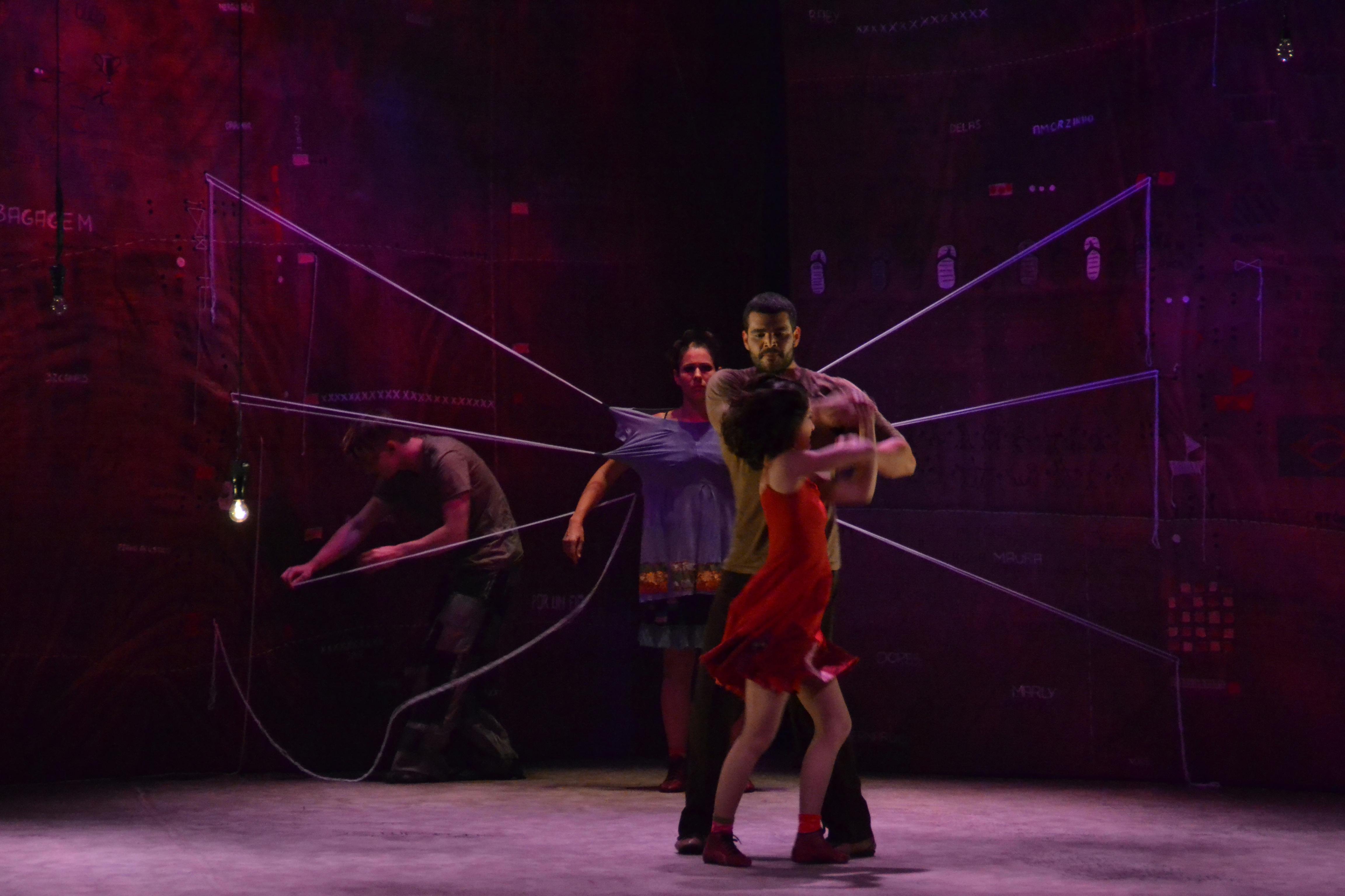 Quattro artisti in scena. Due davanti che ballano. Dietro di loro un danzatore in piedi, indossa sulla schiena una struttura a raggi molto grande.