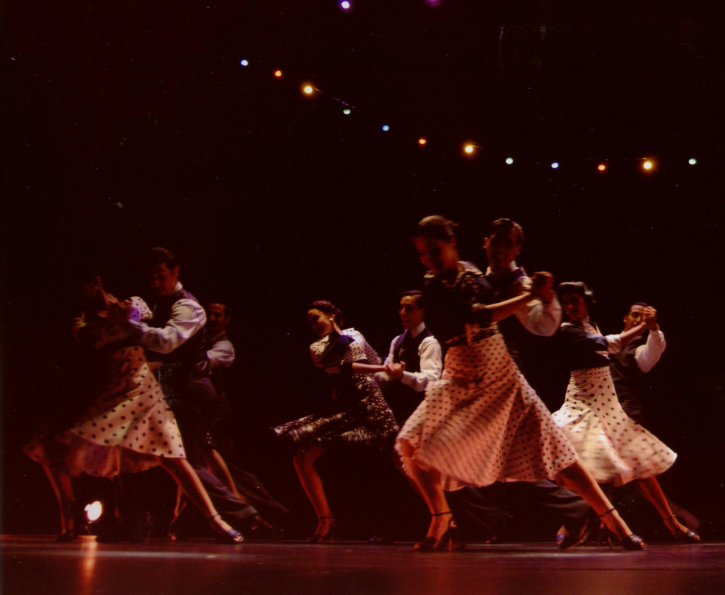 Four couples, man and woman, dance in the same position. They are dressed in outfits for dancing the tango.