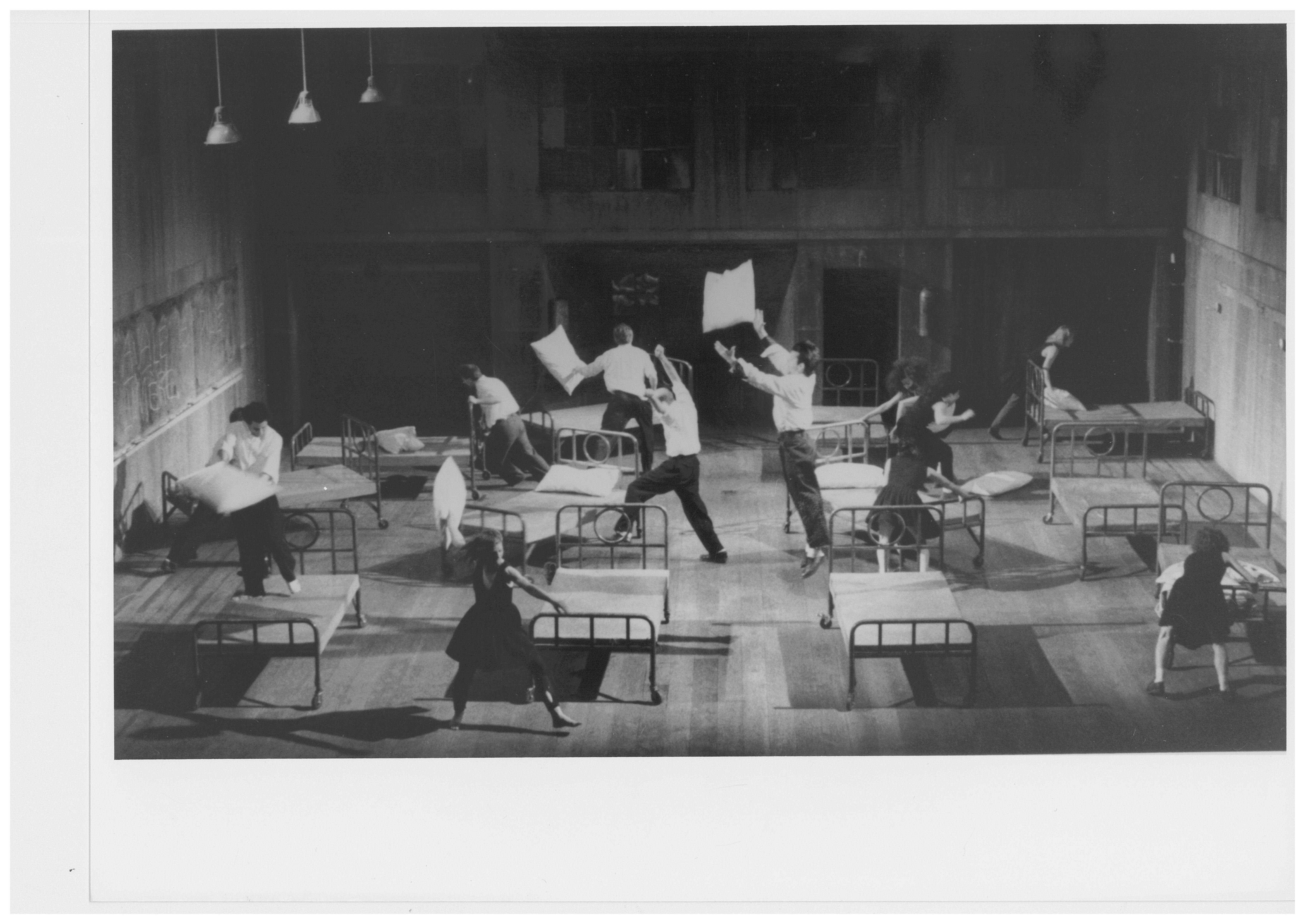 In a room, twelve beds and eleven people running, some with pillows in hand.