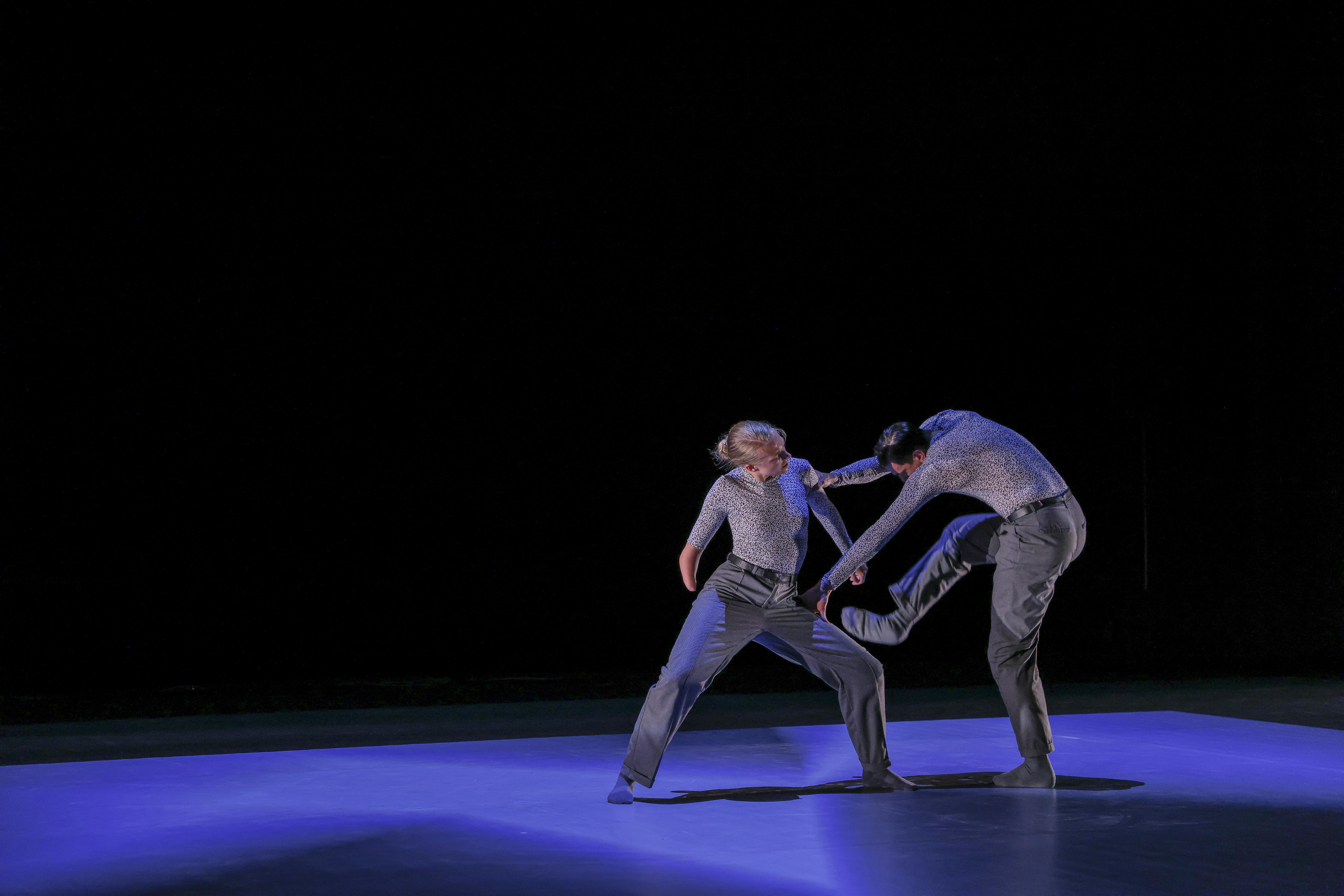 Una danzatrice con disabilità ed un danzatore ballano vestiti di grigio
