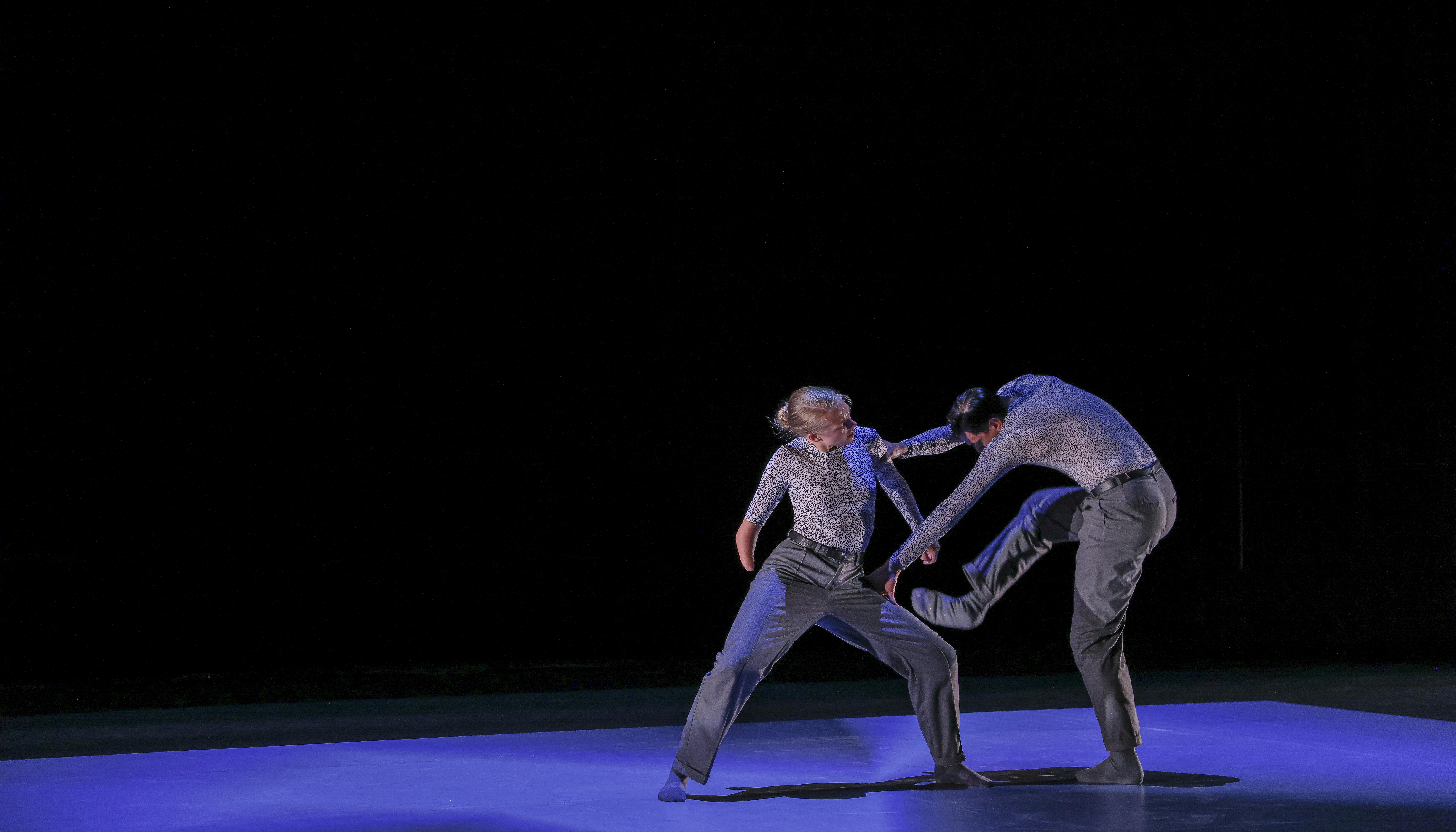 Una danzatrice con disabilità ed un danzatore ballano vestiti di grigio