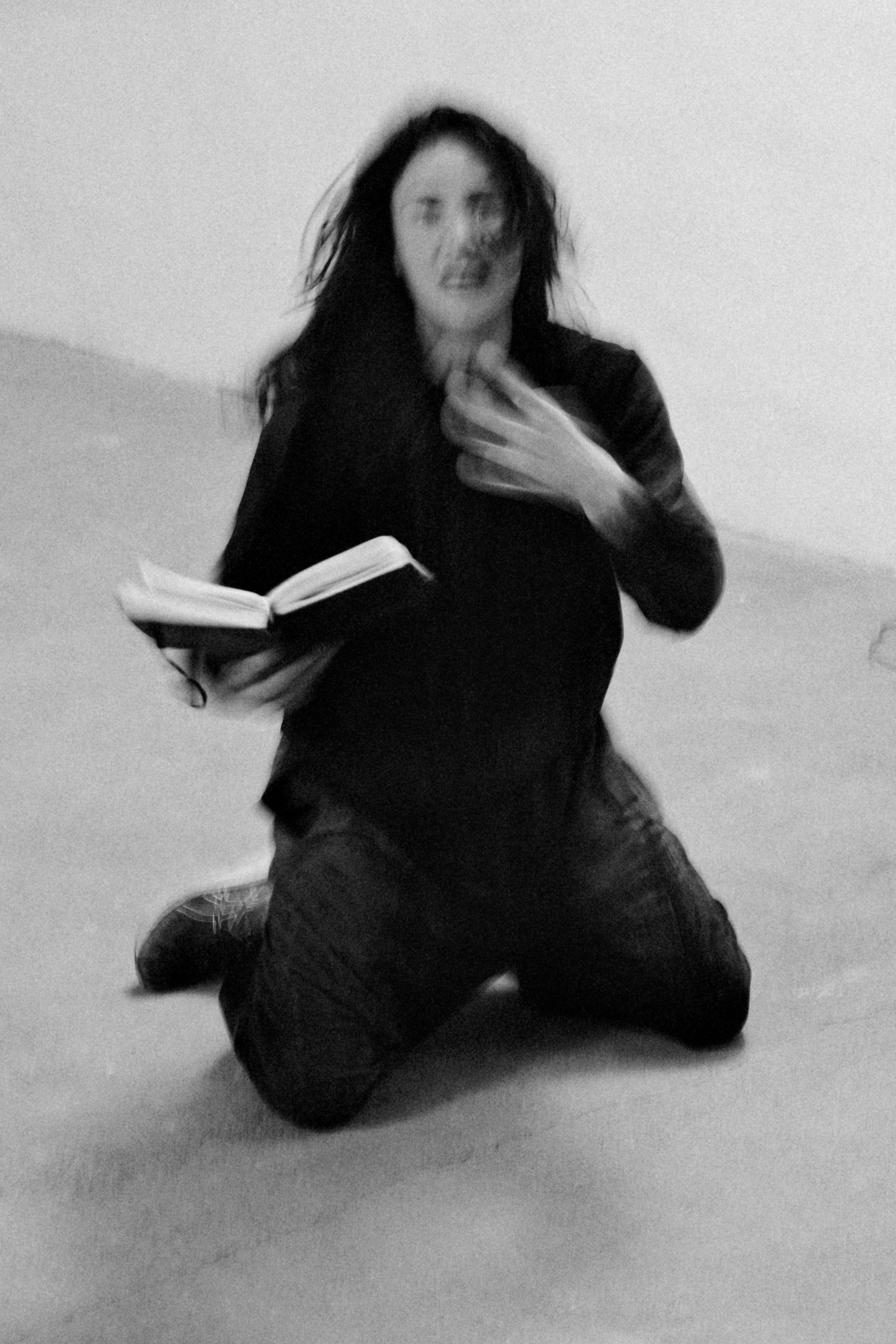Un donna inginocchiata tiene un libro in mano, foto sfocata in bianco e nero