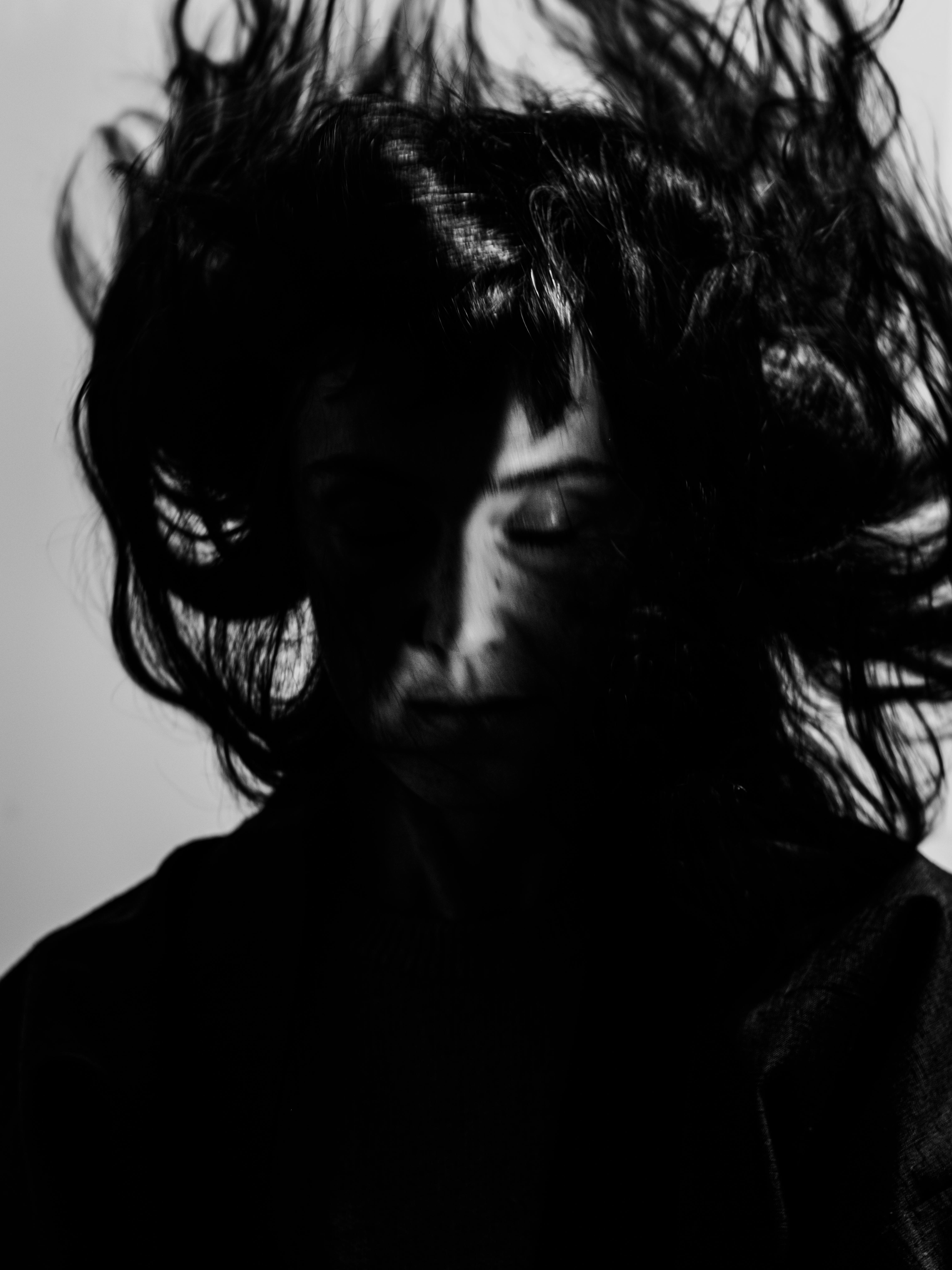 Primo piano in bianco e nero di una donna che tiene gli occhi chiusi i suoi capelli sono in movimento