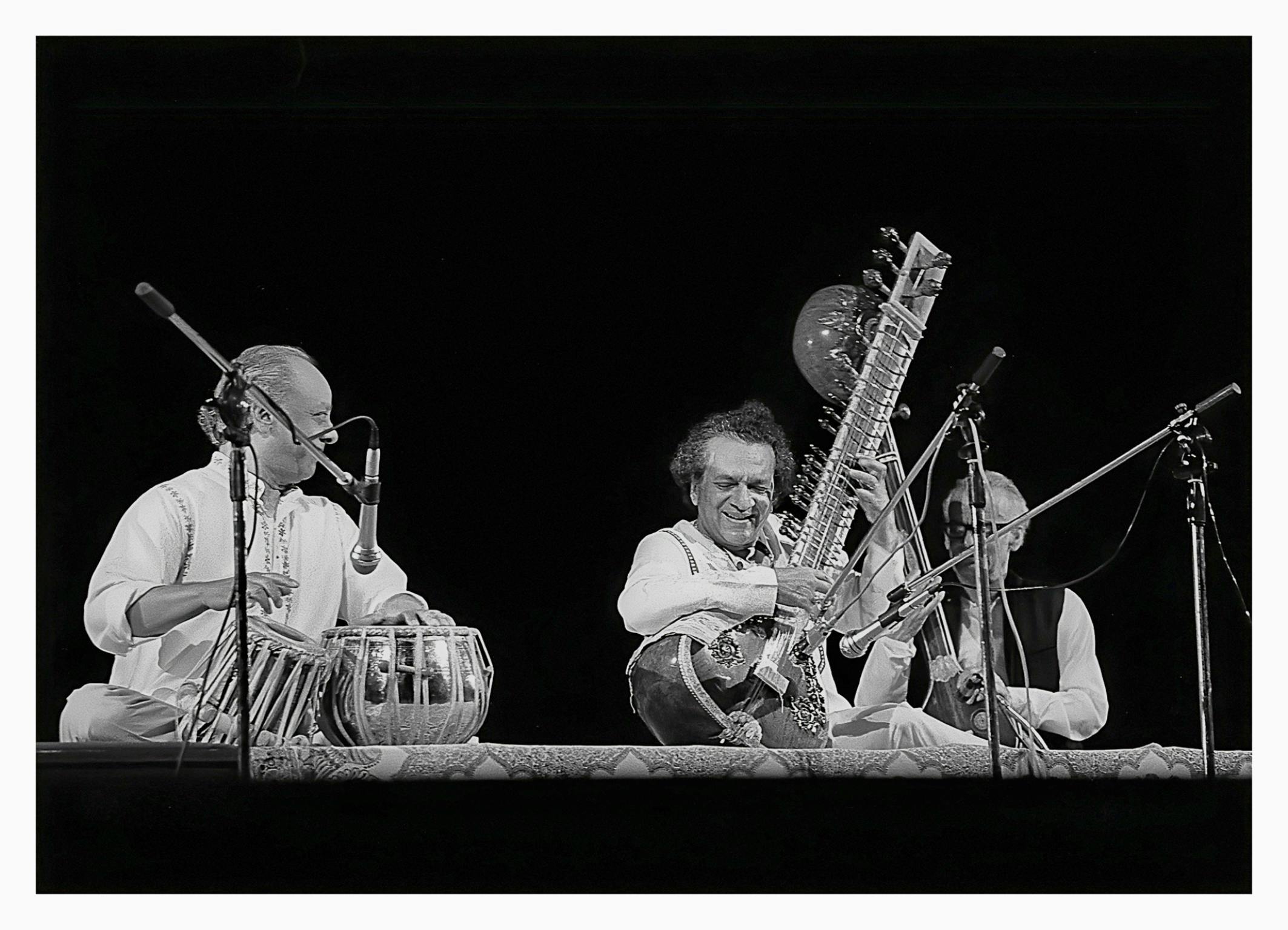 Three musicians on stage, amplified. One plays drums, the other a sitar