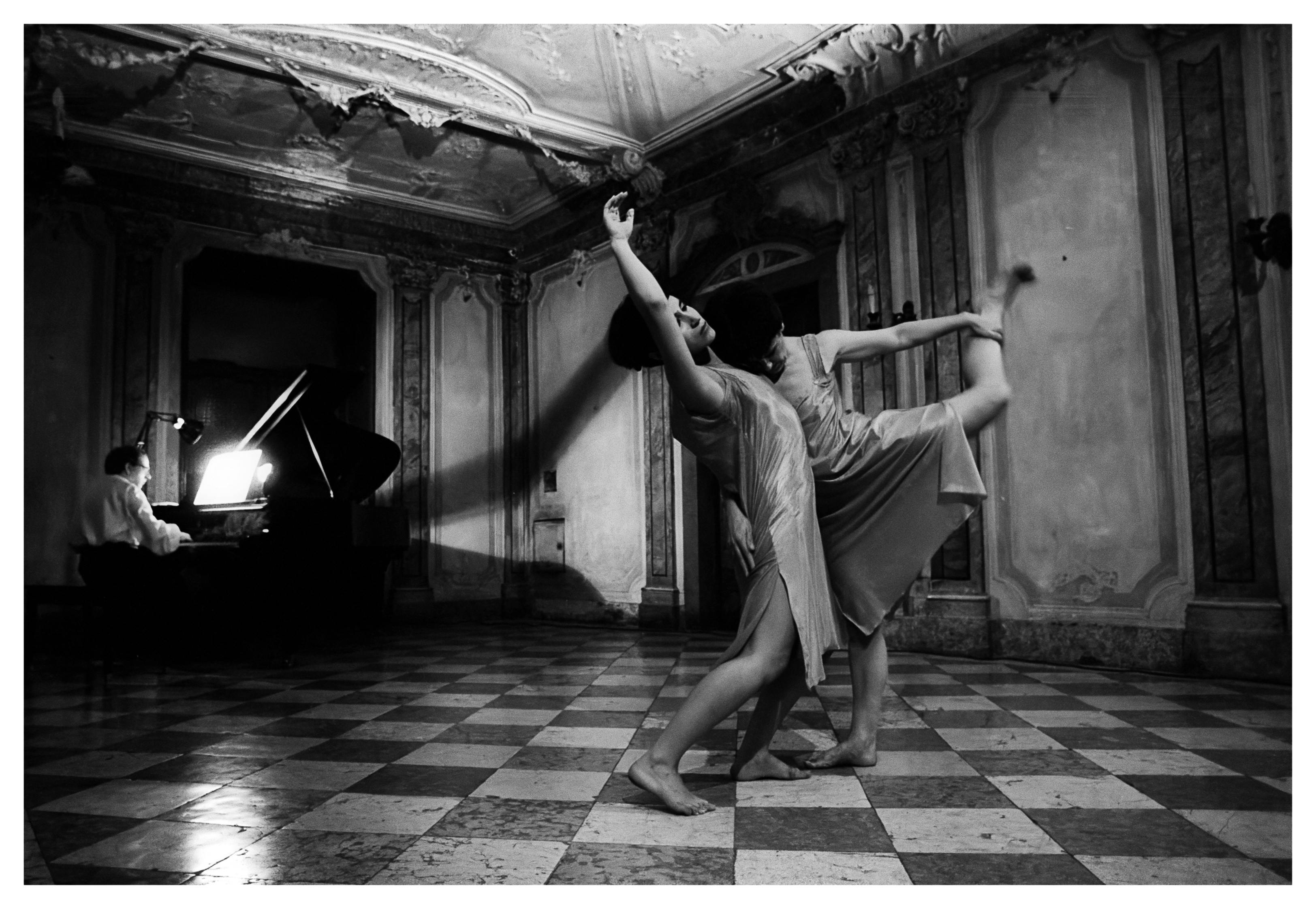 Two dancers dance barefoot, accompanied by the sound of a piano, at the back of the room