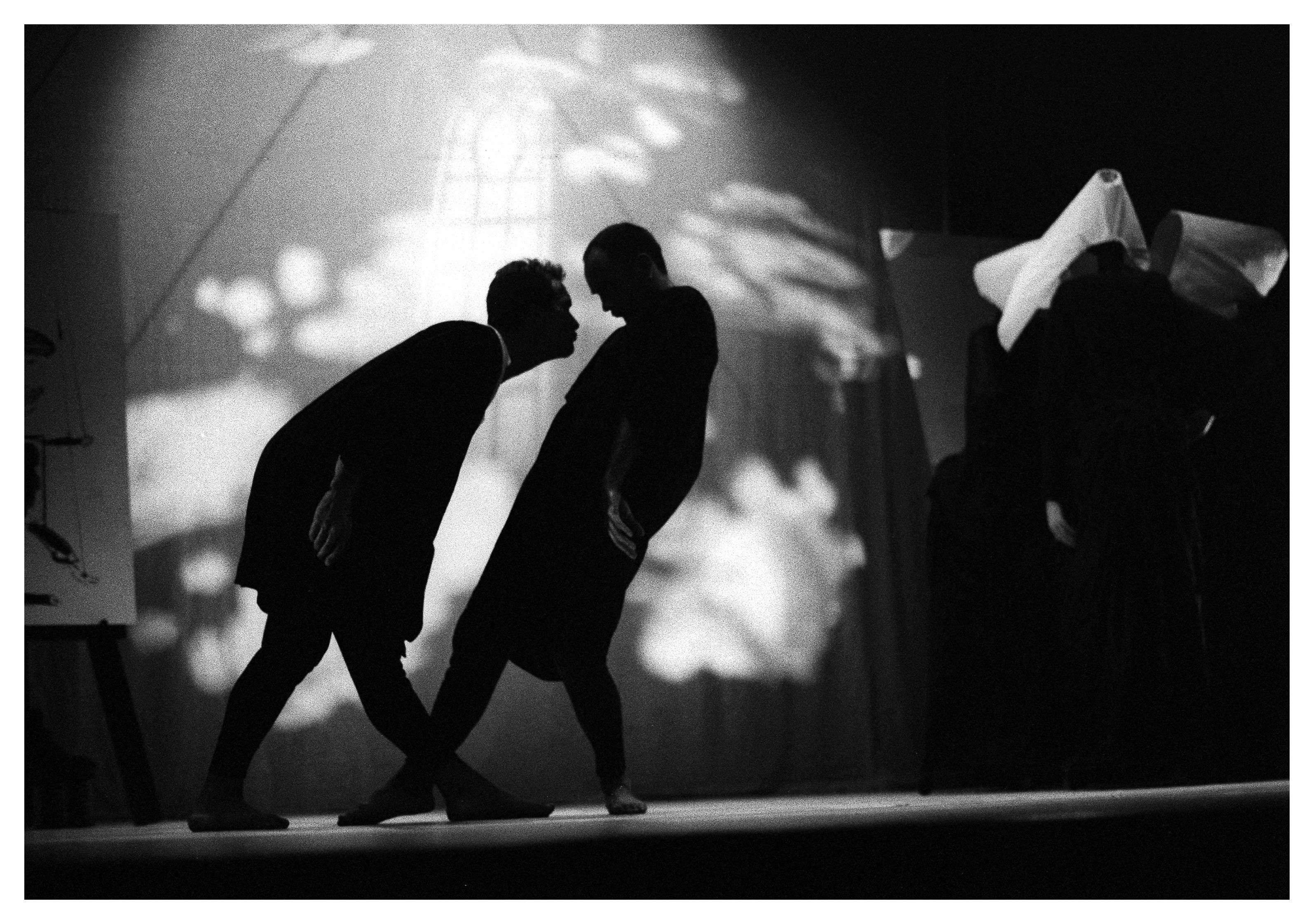 Two people on stage, facing each other. One is leaning towards the other.