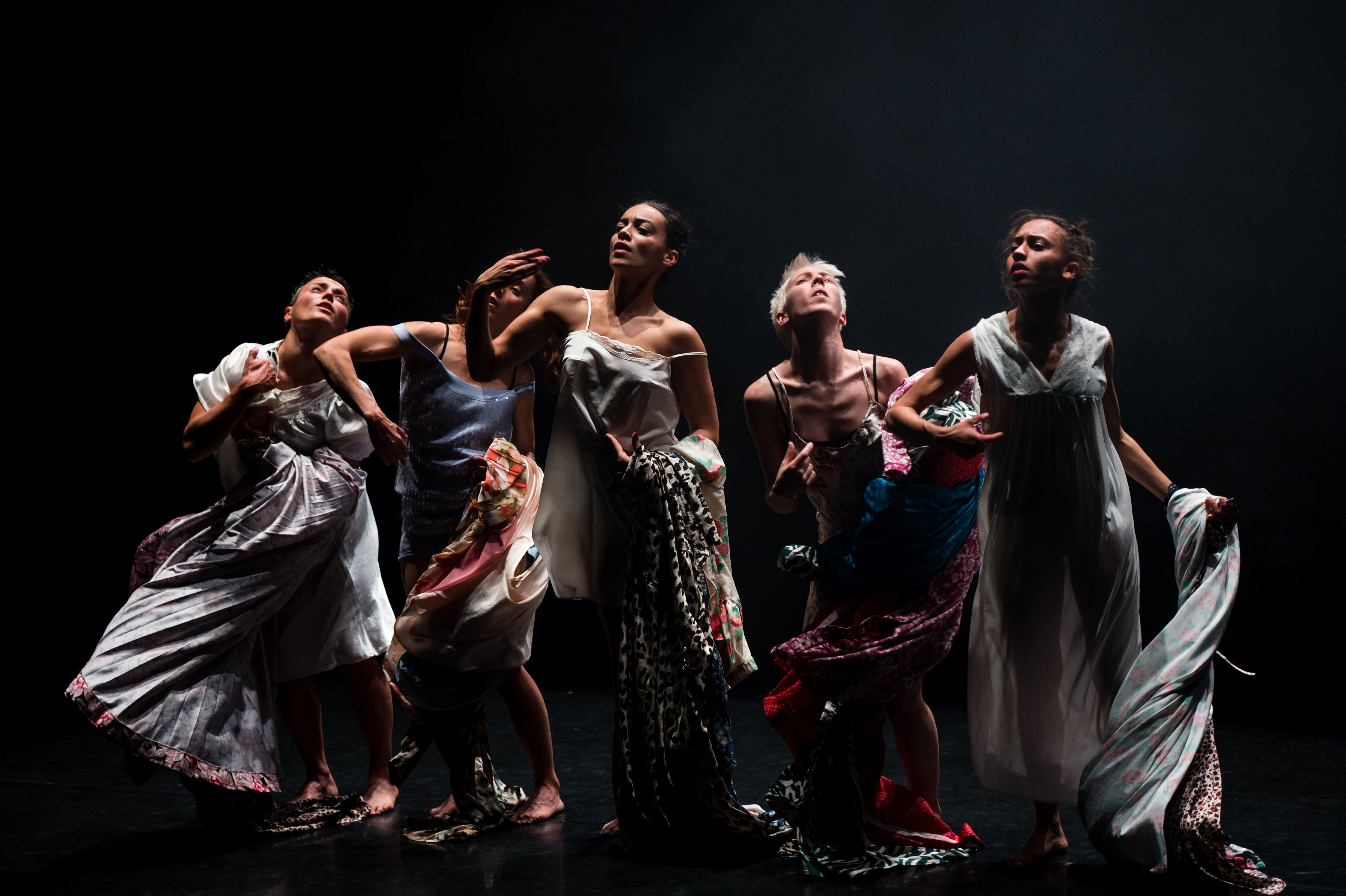 Five dancers dance with their eyes turned upwards. They wear long, colourful dresses