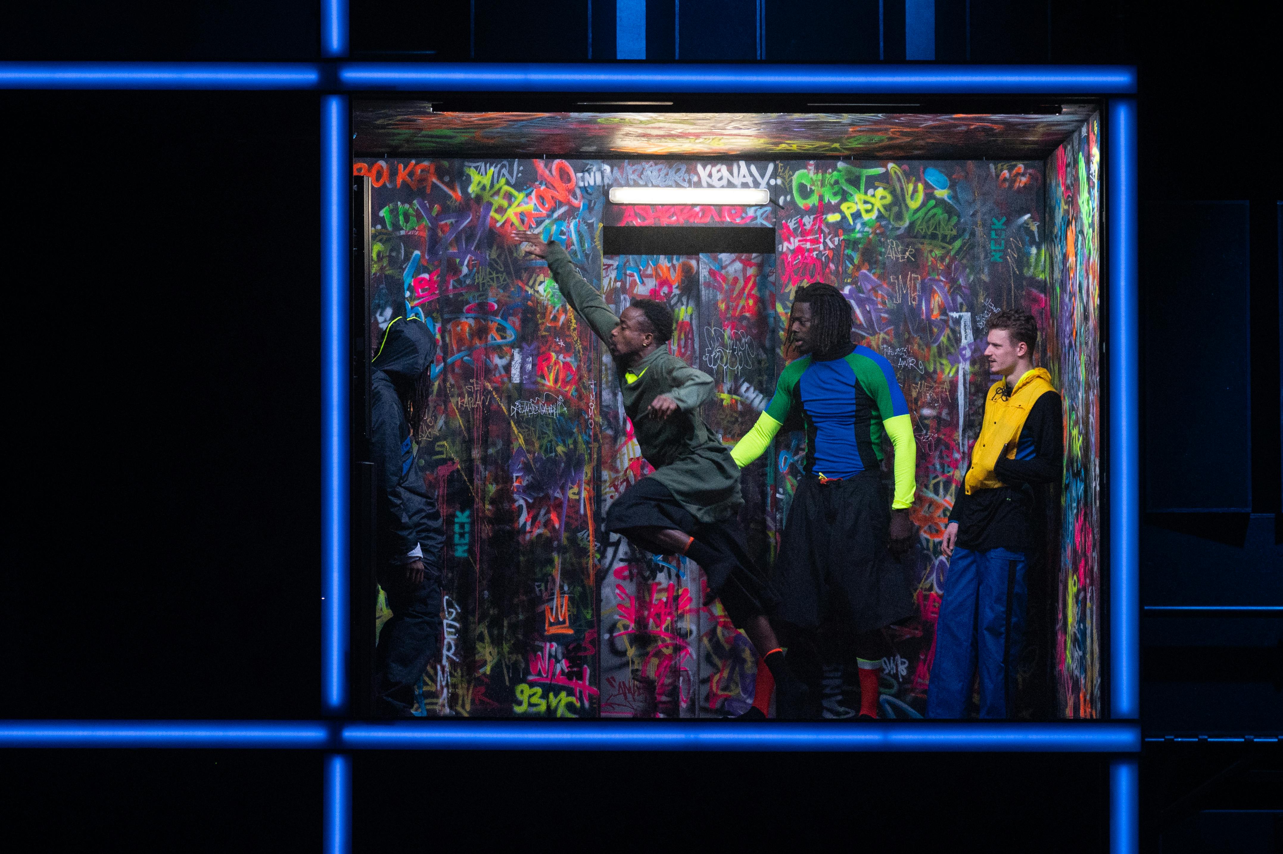 Quattro danzatori ballano in un set con luci al neon e graffiti.